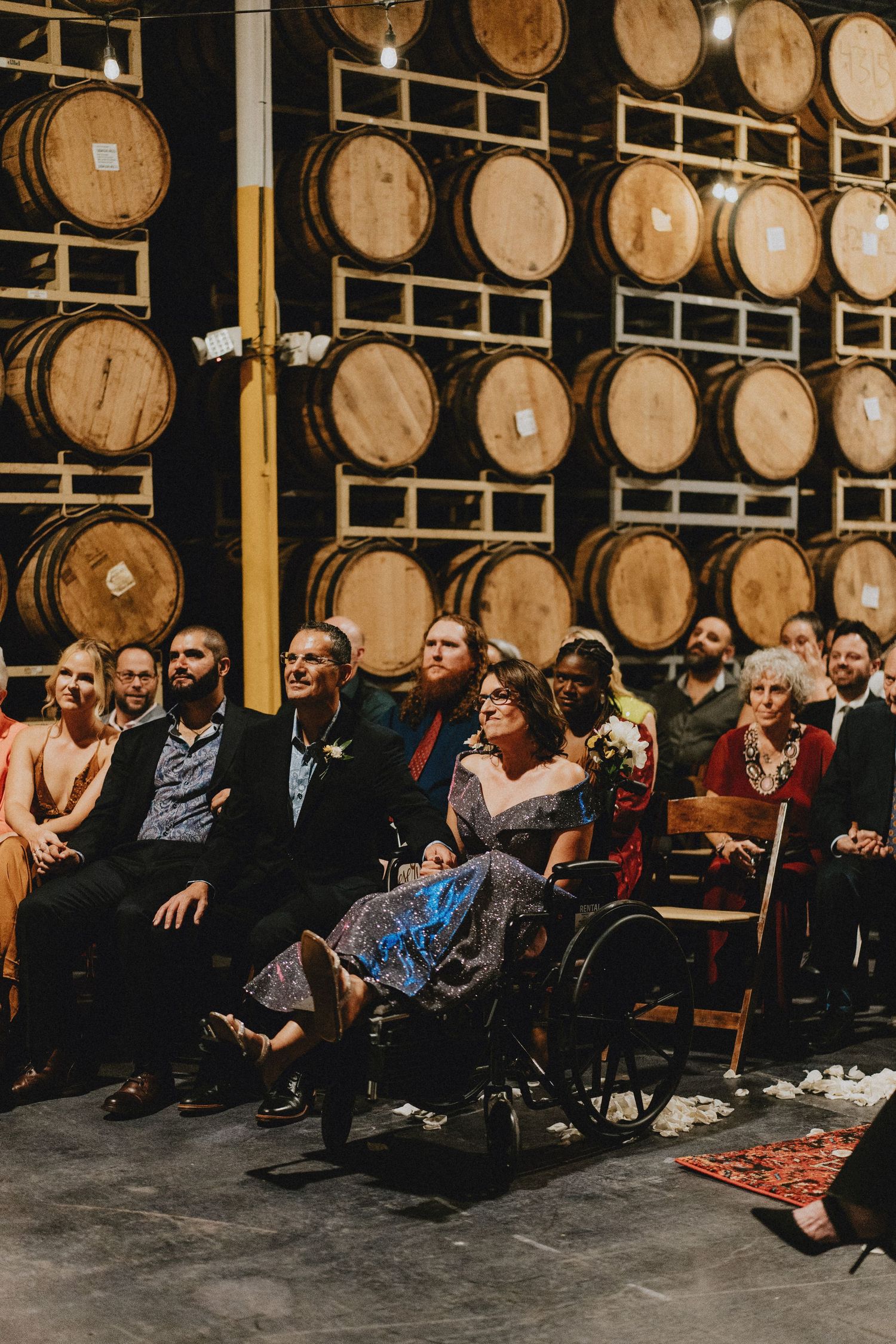 Wedding guests seated before a wall of oak barrels during an elegant winery ceremony celebration.