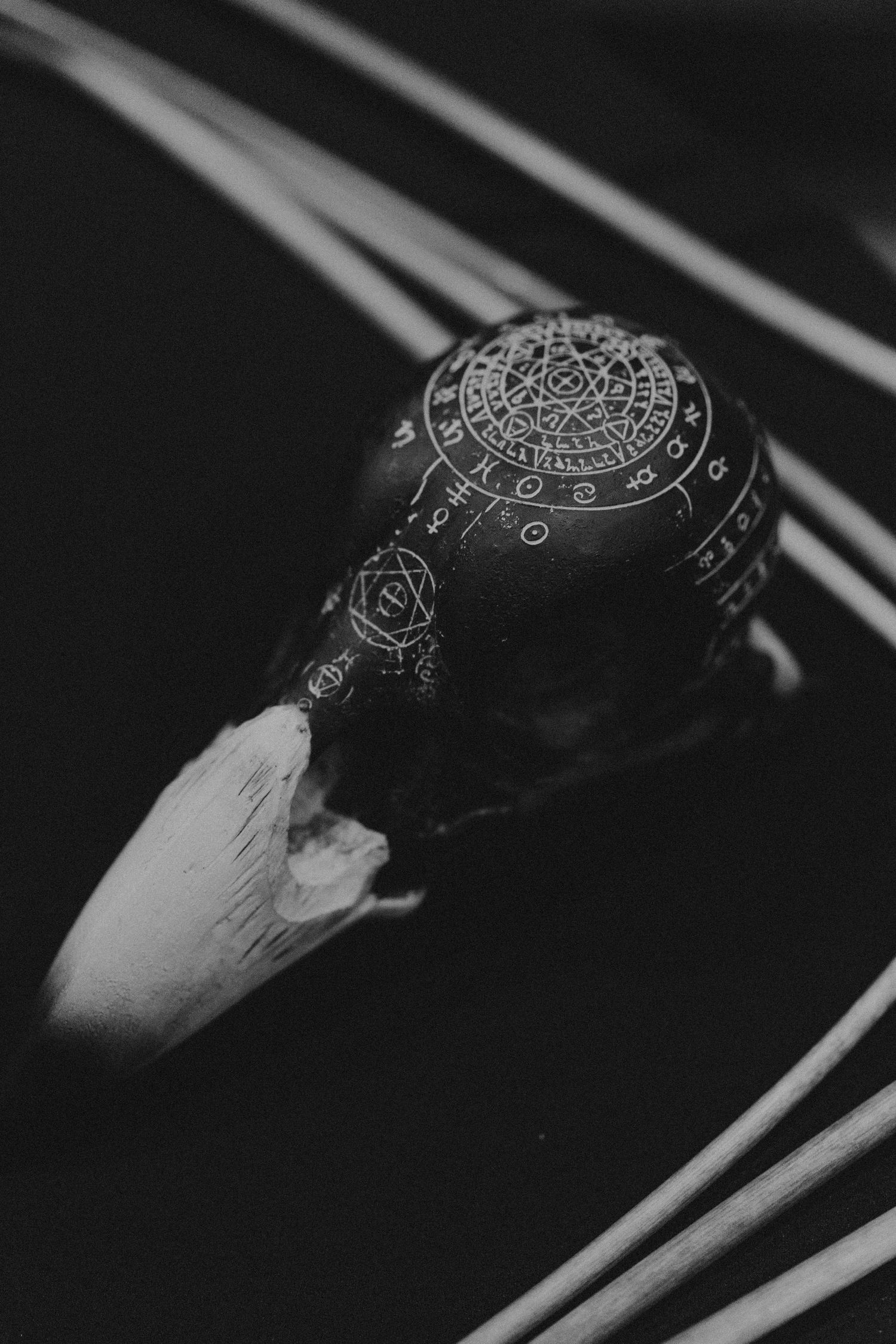 Black and white close-up of an ornate dark ceremonial conch shell engraved with mystical symbols and zodiac designs.