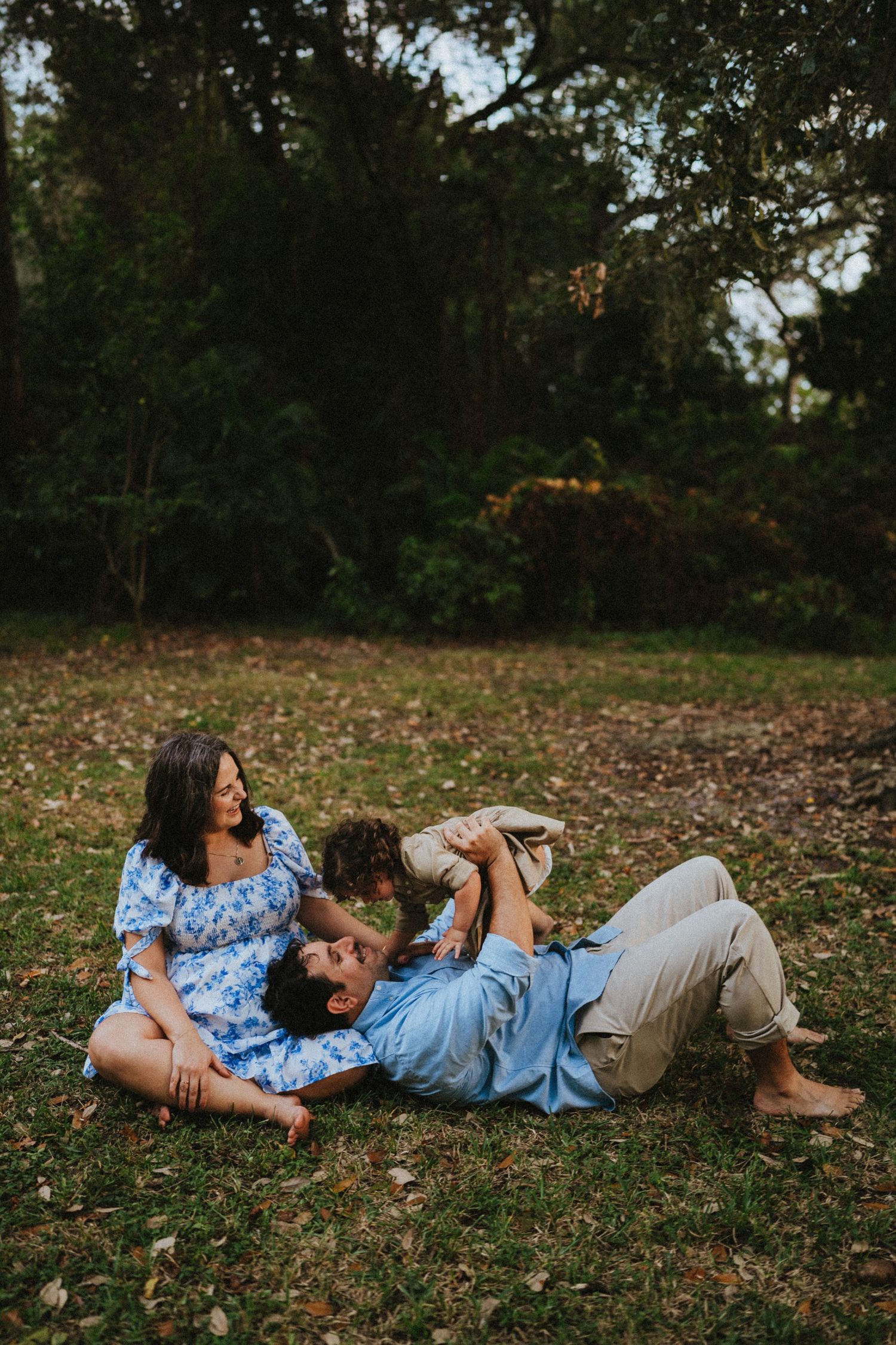 A couple relaxes together on fallen autumn leaves in a wooded park setting at dusk.