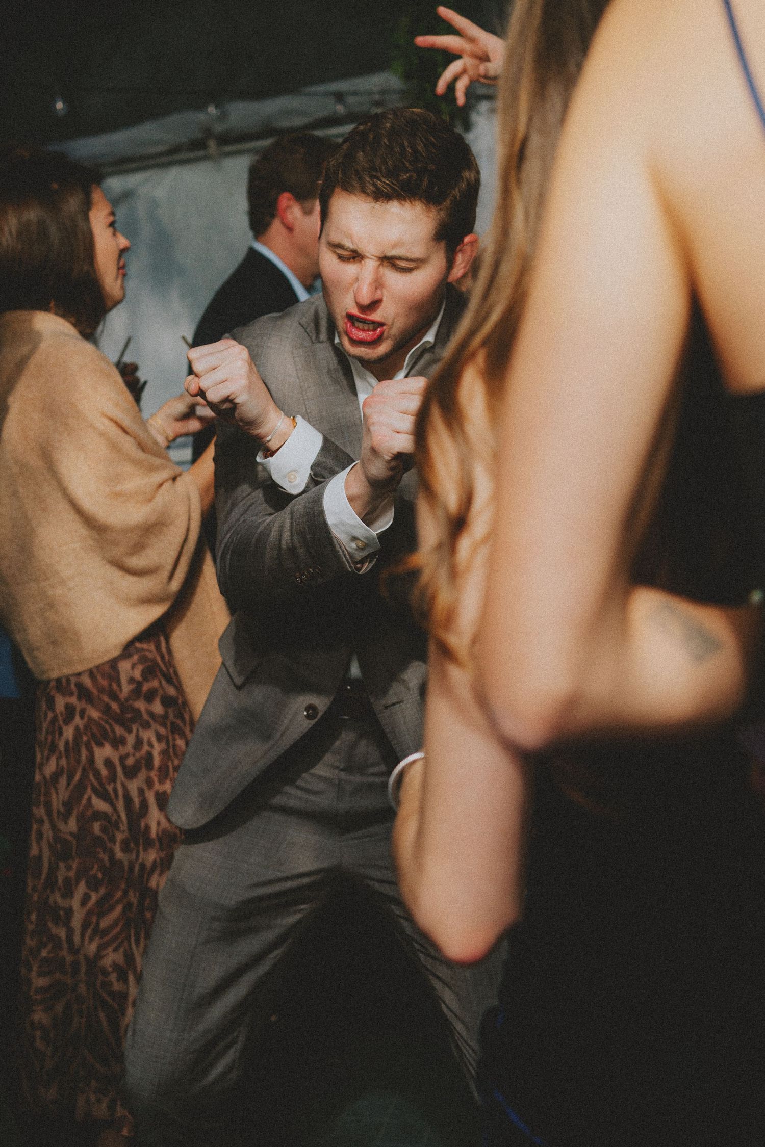 Energetic wedding guest in gray suit dancing enthusiastically on the crowded reception dance floor.