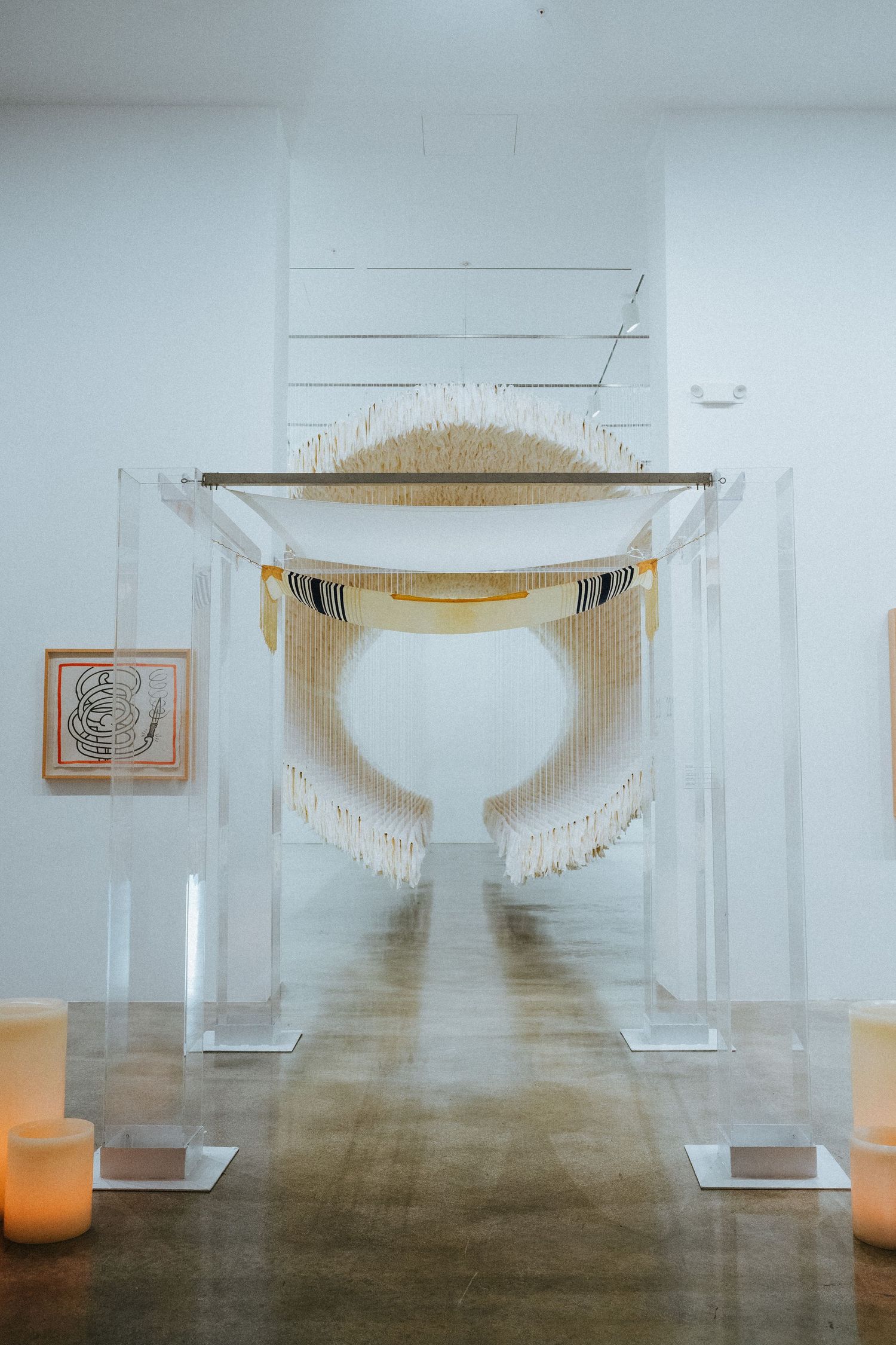Modern wedding chuppah with white fringe macrame on acrylic stands in a minimalist gallery space.