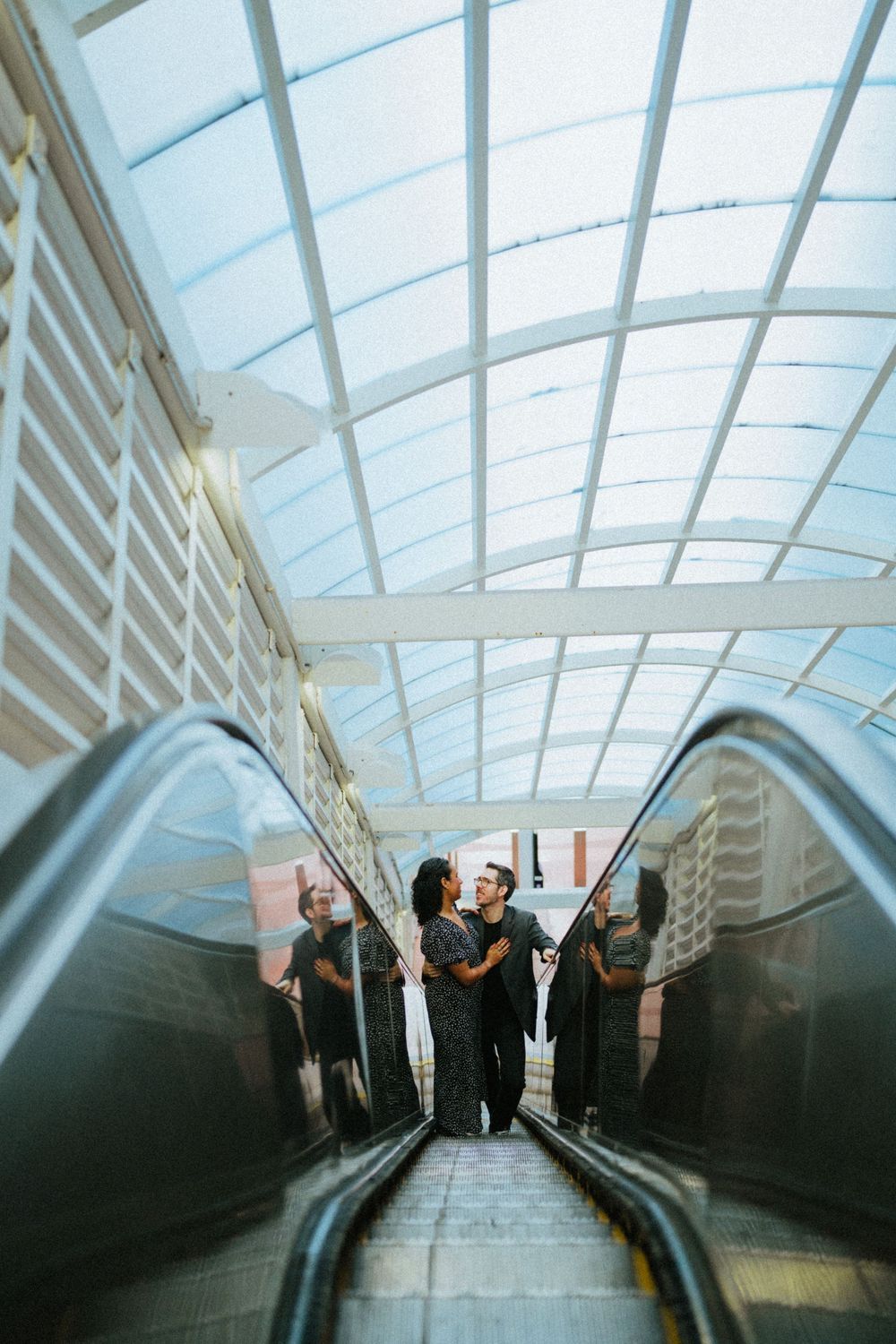 Group ascending illuminated escalator under curved glass ceiling.