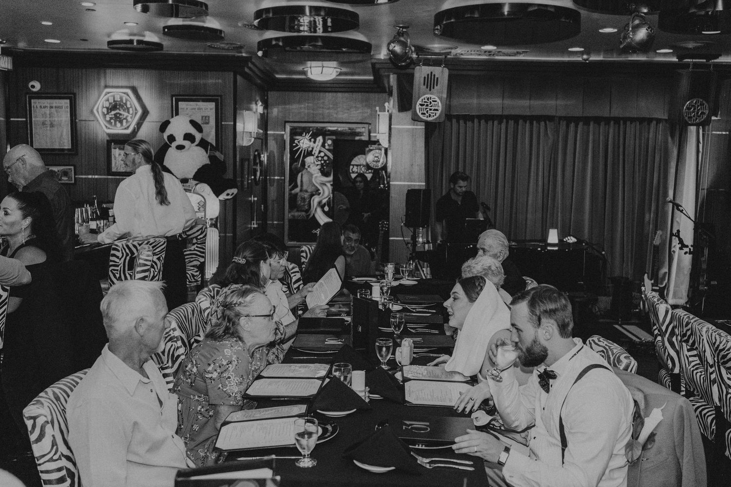 Black and white photo of guests dining at a long table with a costumed character at a restaurant.
