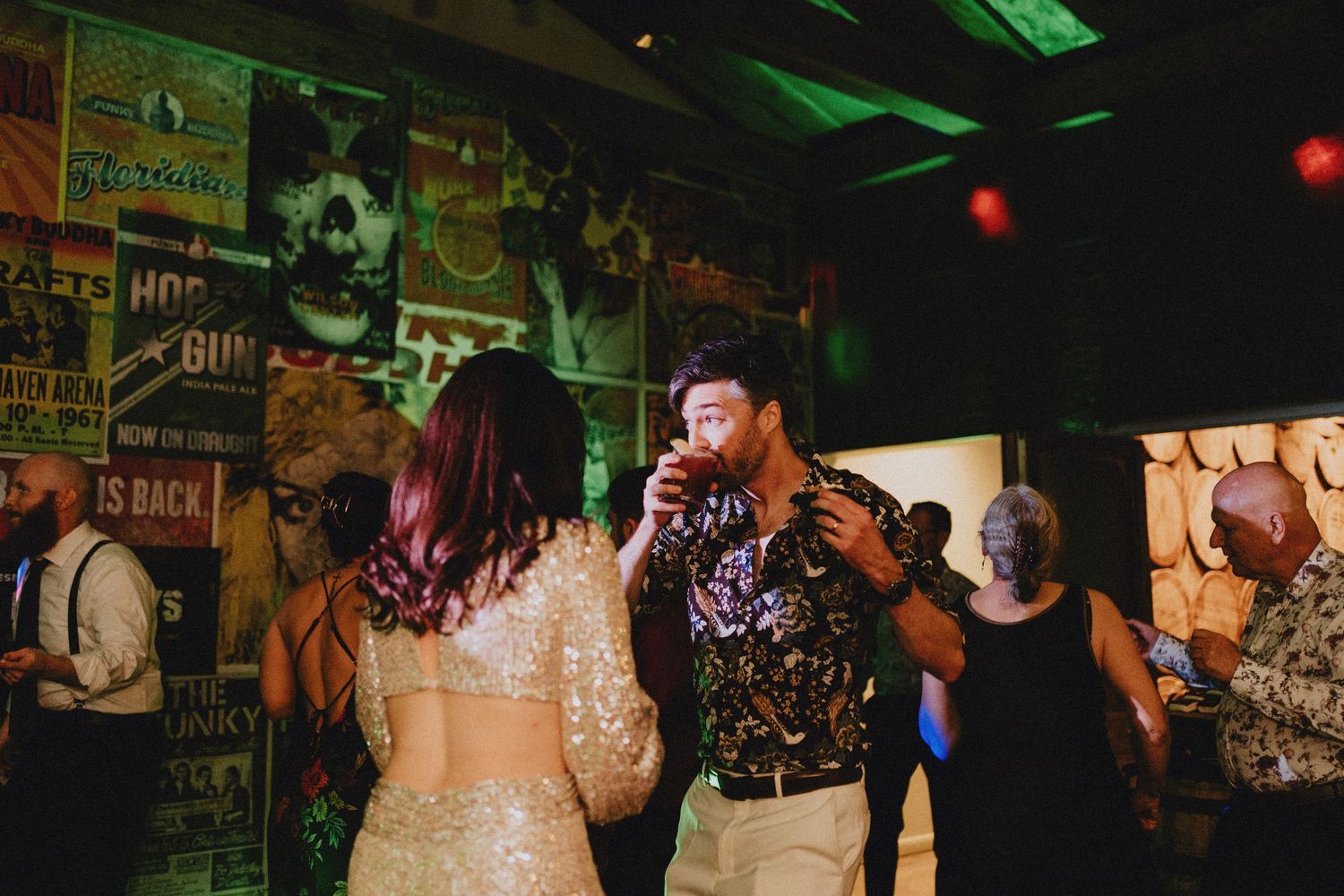 Couple dancing and drinking at a lively wedding reception with eclectic vintage poster decor.