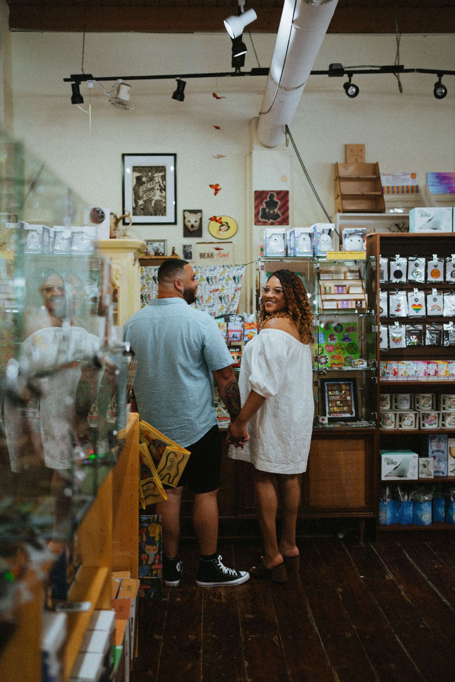 Couple holding hands and smiling in a charming gift shop with wooden floors and colorful merchandise displays.