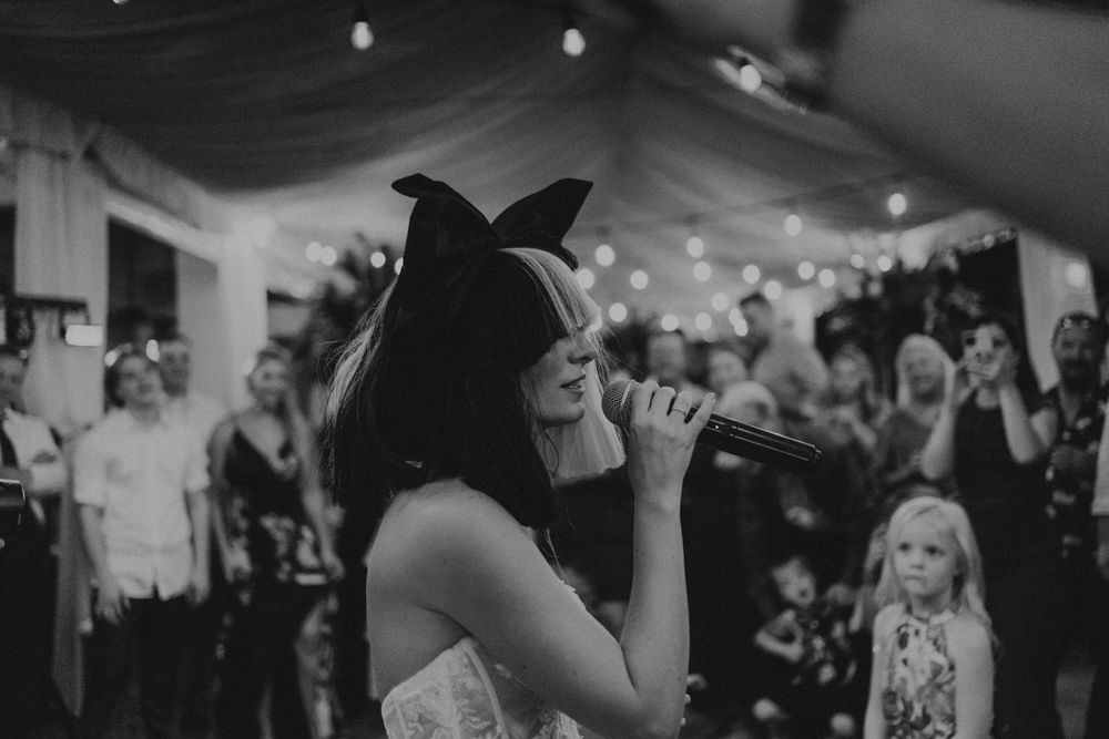 Black and white photo of a lively wedding reception dance floor with string lights.