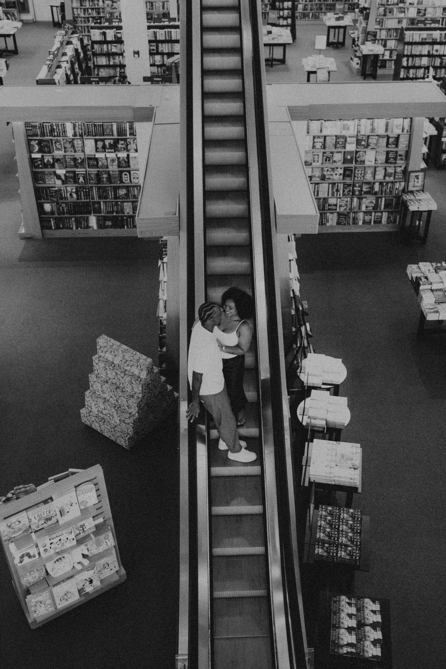 Couple embracing on escalator in bookstore, aerial black and white photo.