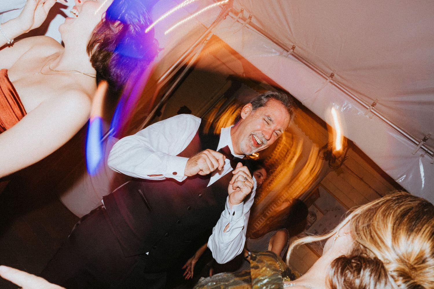 Joyful groom dancing energetically at wedding reception under warm glowing lights.