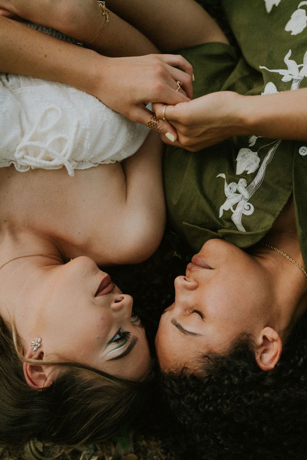Overhead view of two people lying on grass holding hands with contrasting outfits.