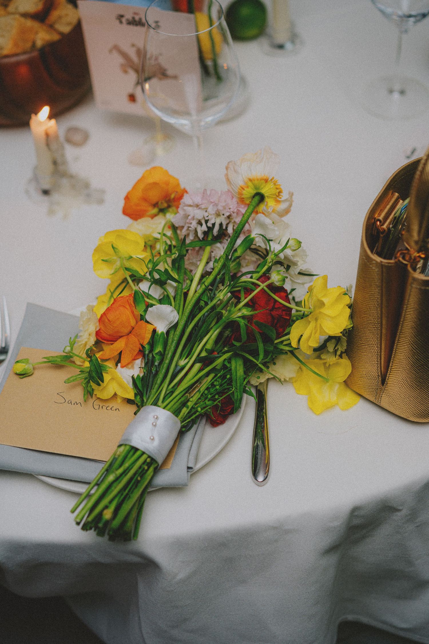 Vibrant mixed wildflower bouquet with yellow, orange, and red blooms on a white tablecloth at a formal dinner.