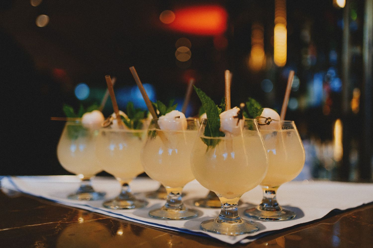 Row of elegant cocktails garnished with mint and straws on a bar tray in a dimly lit upscale bar.