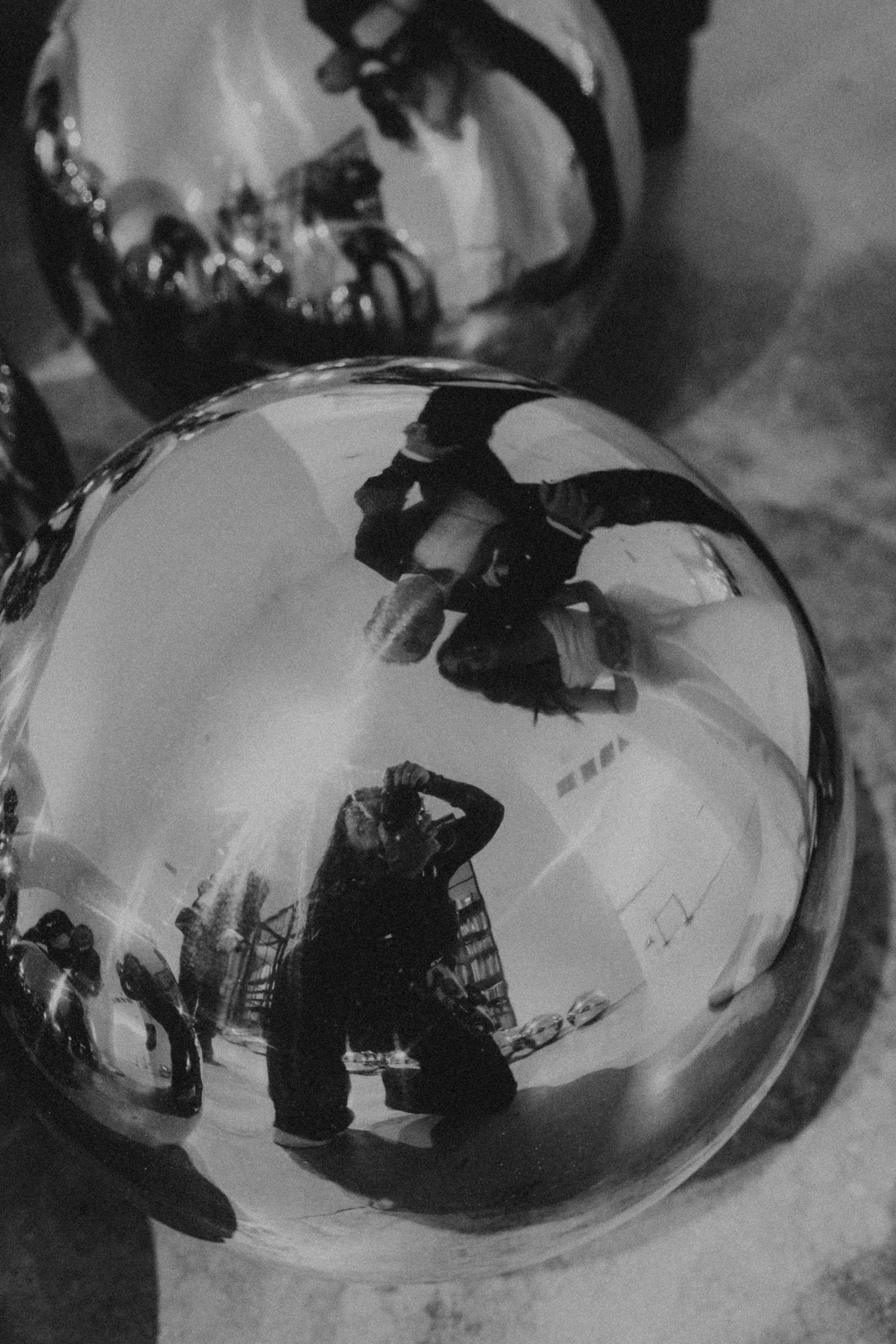 Black and white photo of reflective metallic spheres capturing a distorted mirror selfie of a photographer.