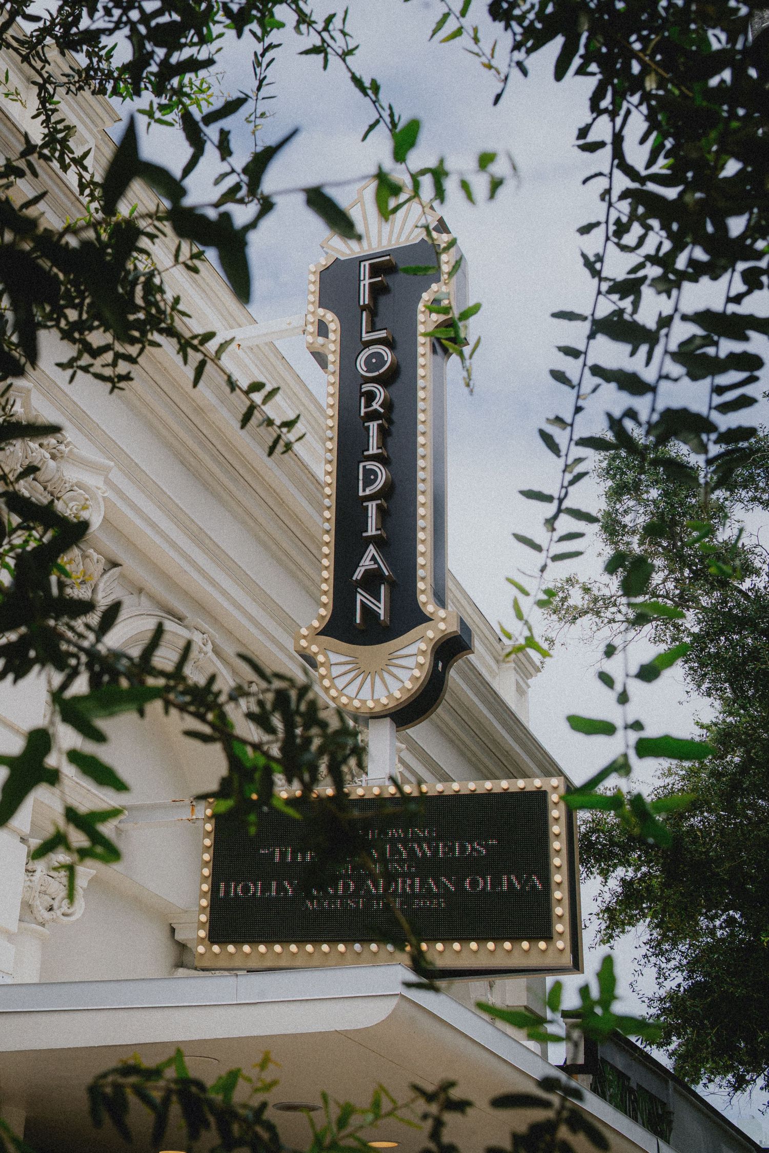 Florian theater marquee sign announcing newlyweds Holly and Adrian Oliva wedding, framed by green leaves.
