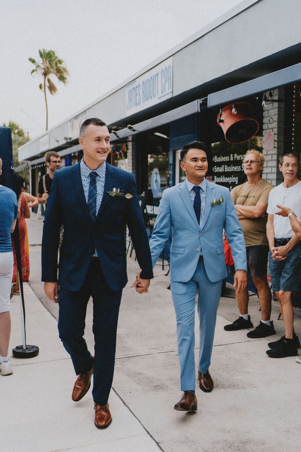 Group walking along a storefront wearing light blue and navy suits with brown dress shoes.