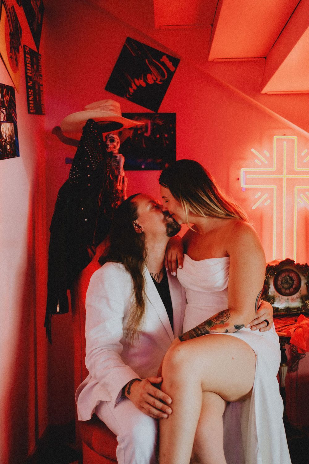 Intimate moment captured in red lighting with neon cross decoration in background.