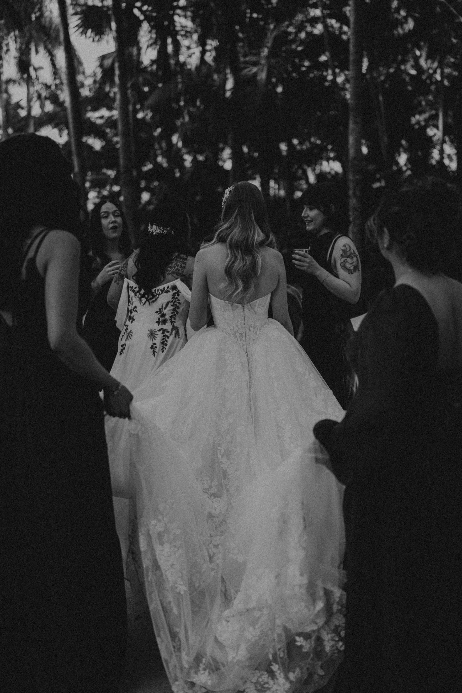 A series of dark and moody wedding photos showing people in black attire and white dresses walking through trees at dusk.