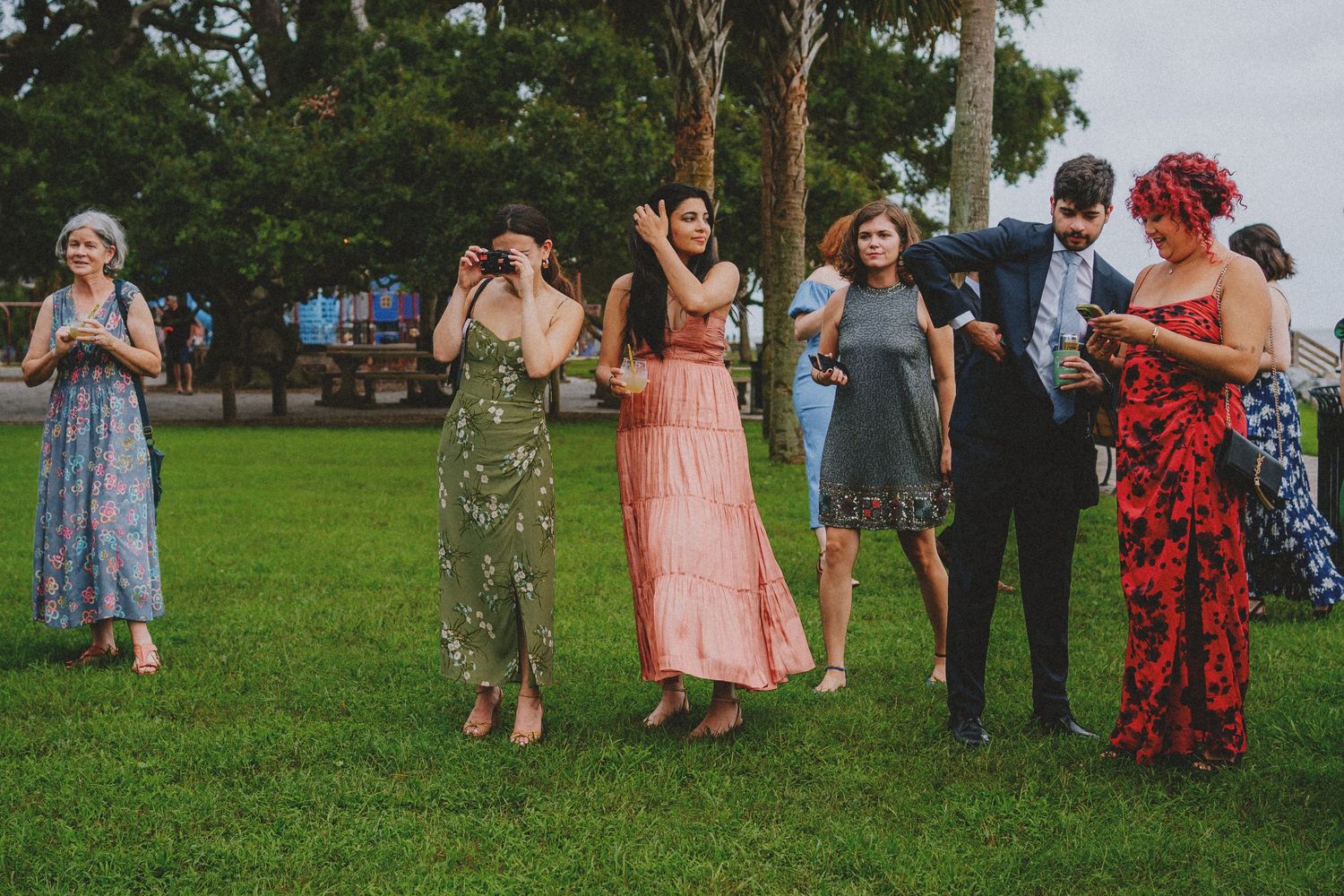 Guests in colorful formal dresses socializing on green lawn at outdoor wedding celebration.