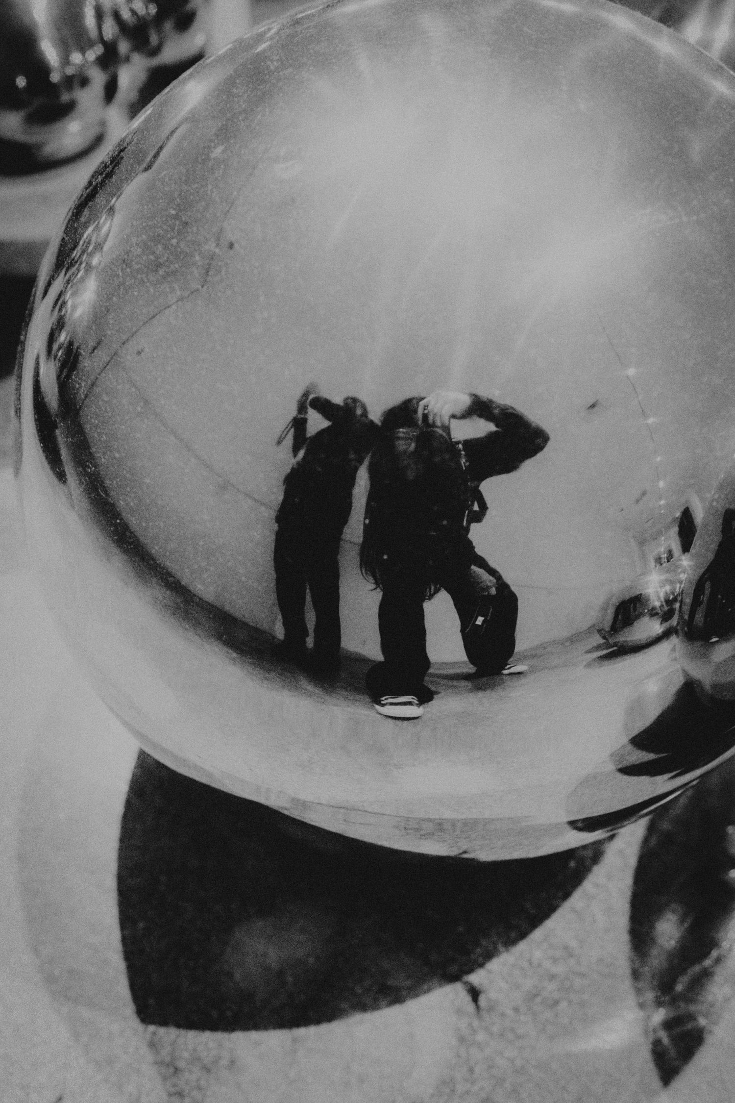 Black and white reflection of two people in a shiny metallic sphere, captured in artistic monochrome photography.