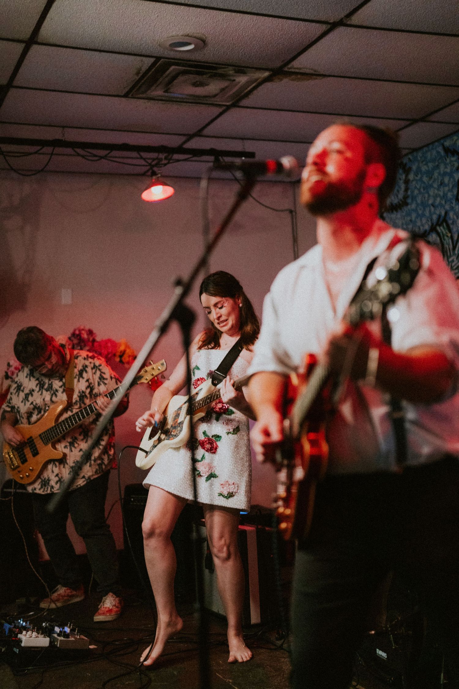 Live band performing on stage with guitarist and bassist in colorful shirts under warm red lighting.