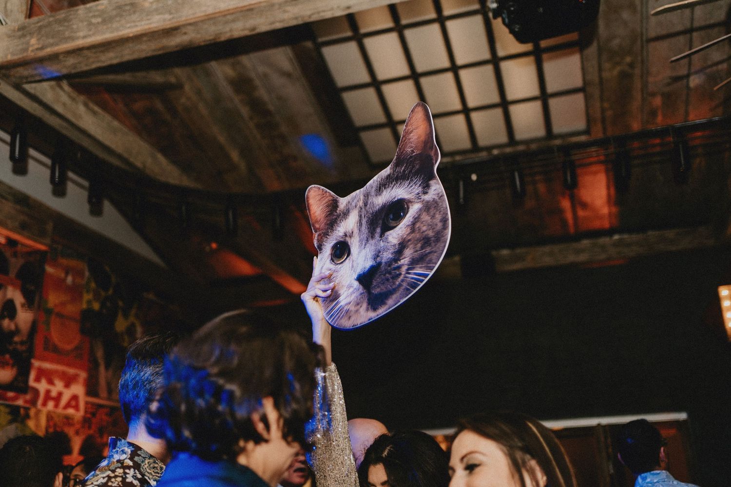 Guest holding up a large cat face photo prop above the crowd at a festive wedding reception.