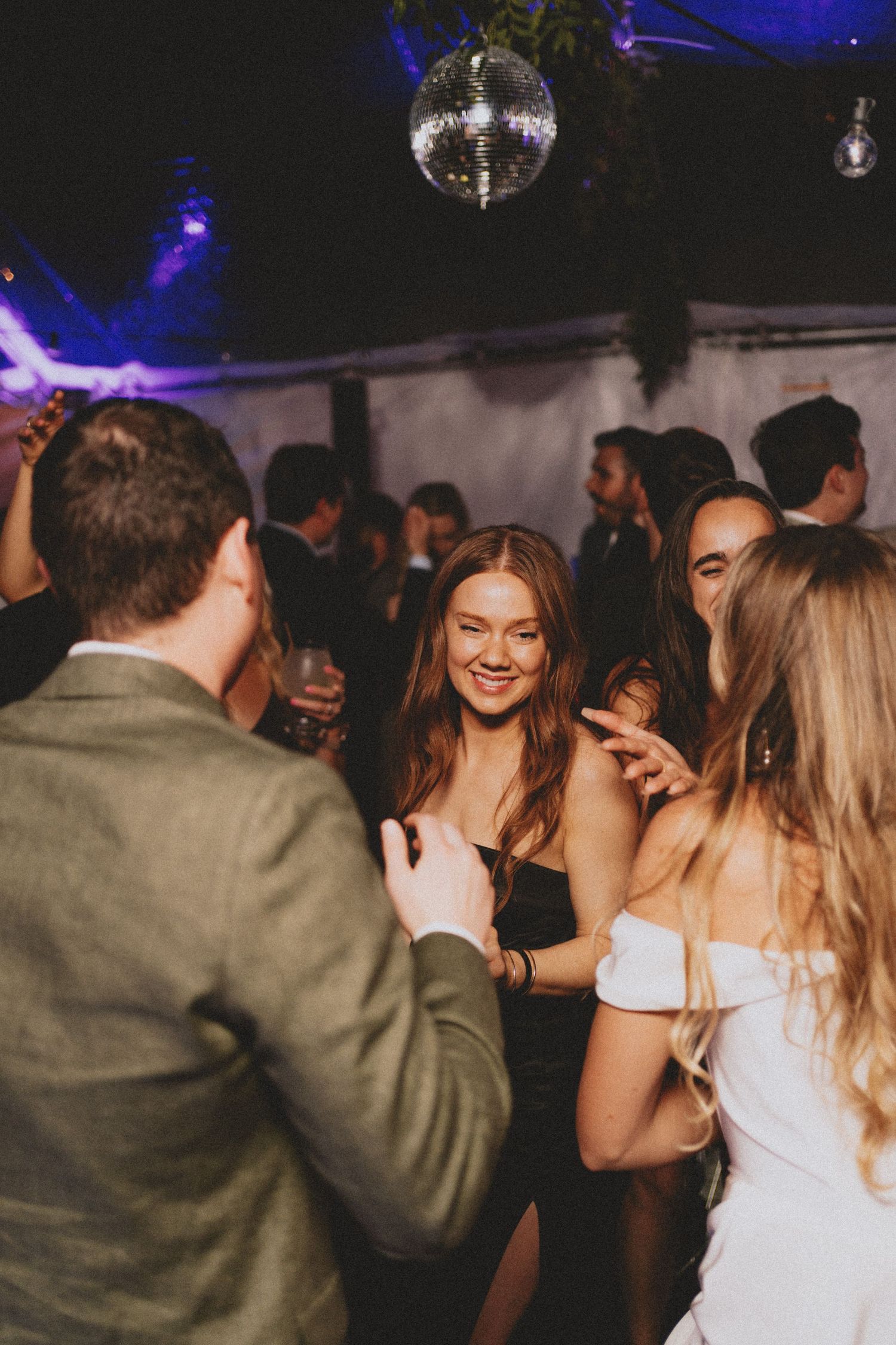 Wedding guests dancing under a disco ball at a lively outdoor evening reception party.