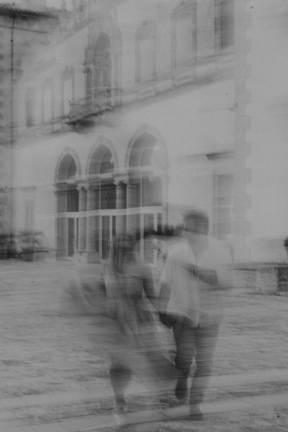 A blurred vintage photograph capturing movement along an ornate building exterior.