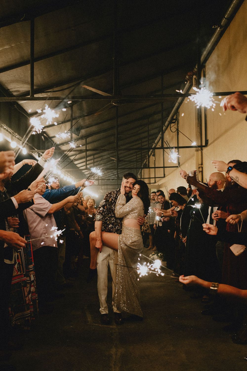 Wedding guests holding sparklers creating a tunnel of light during evening celebration.