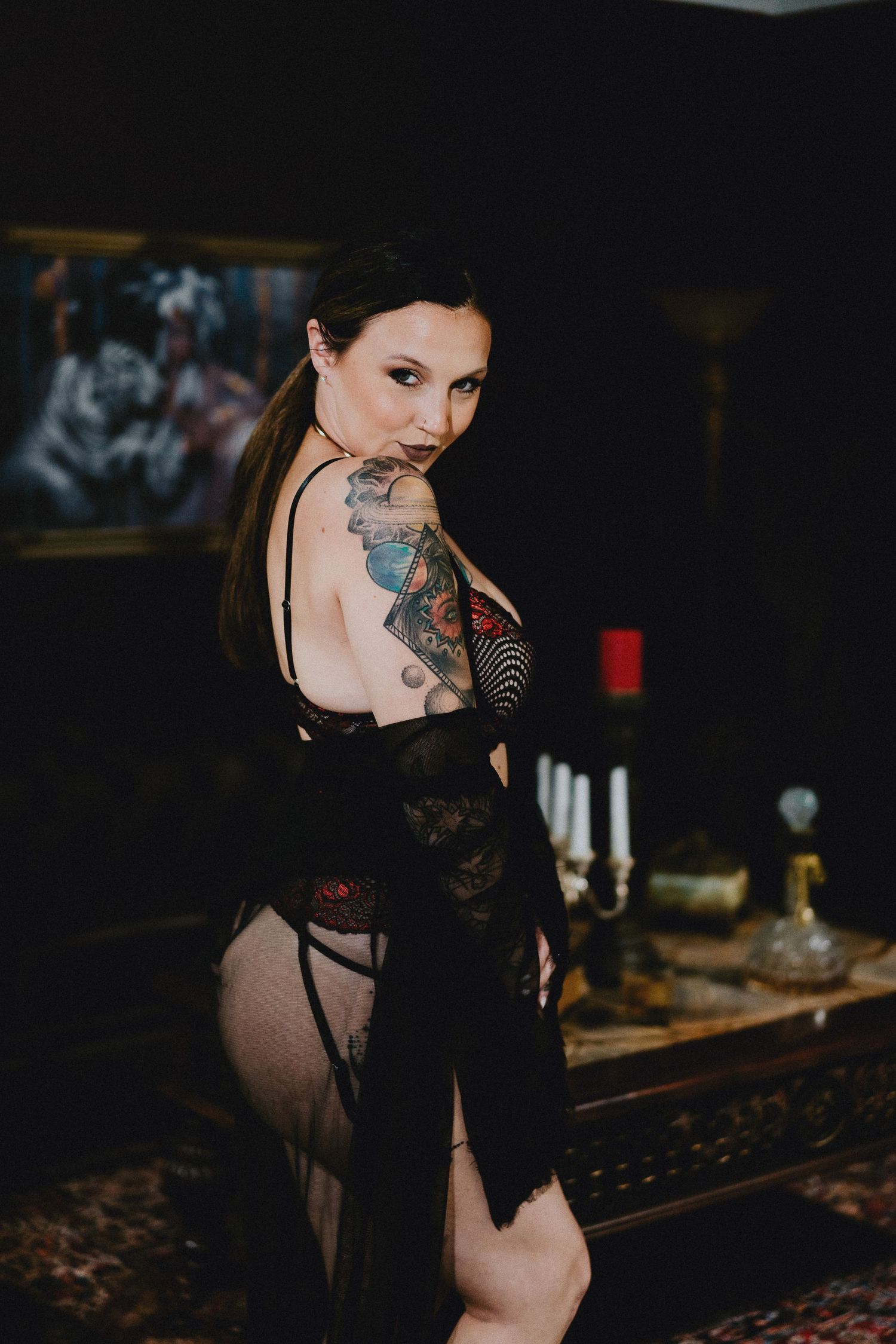 Model in black lace dress shows ornate tattoos in moody lighting.