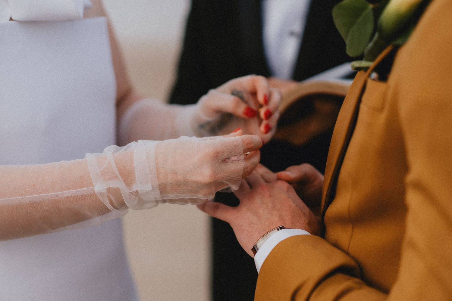 Bride placing a wedding ring on grooms finger during ceremony, close-up of hands.