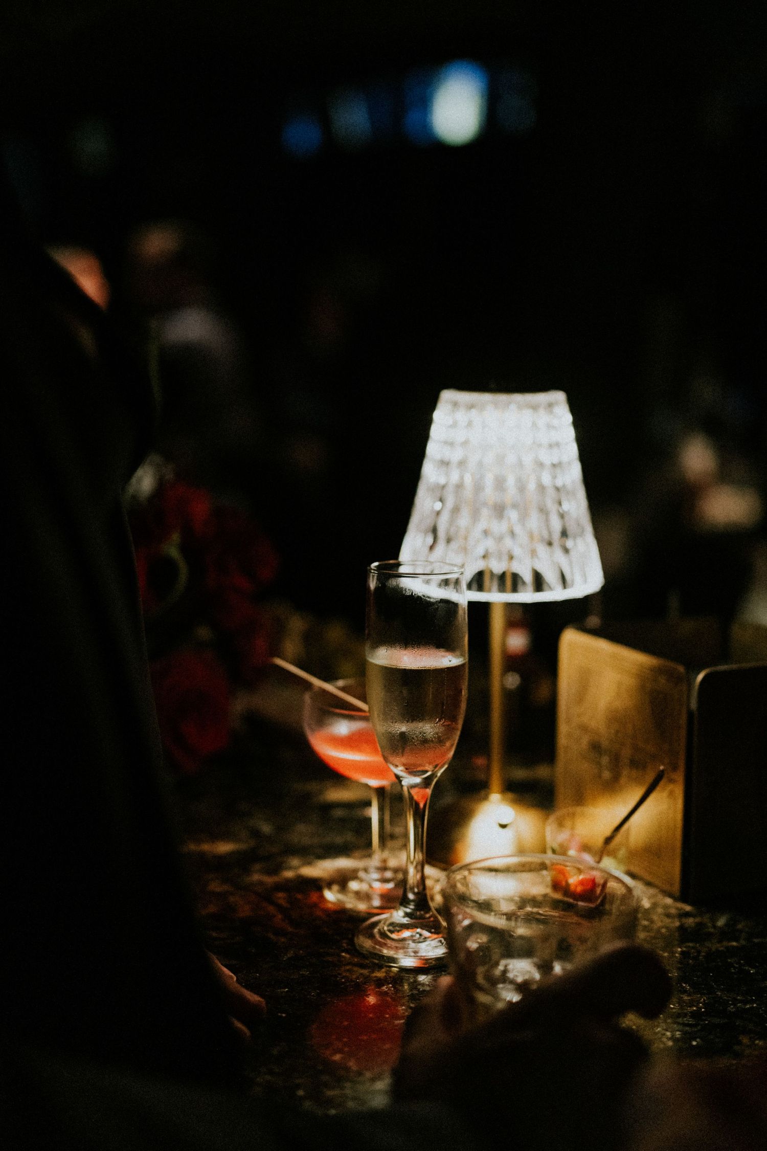 Elegant champagne flute and pink cocktail beside a glowing crystal table lamp at wedding reception.