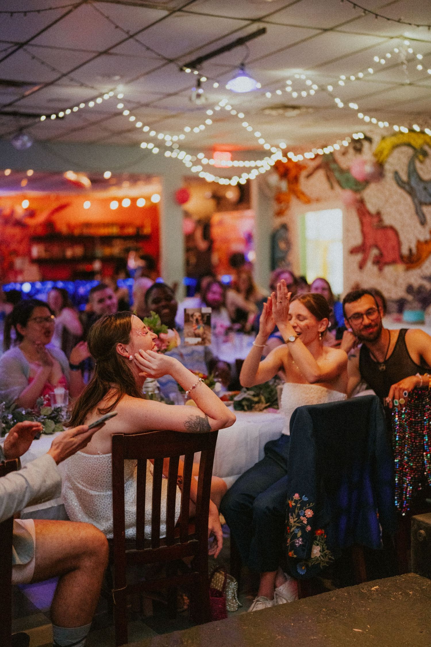Bride and guest sharing a joyful high-five moment at a vibrant wedding reception with string lights.