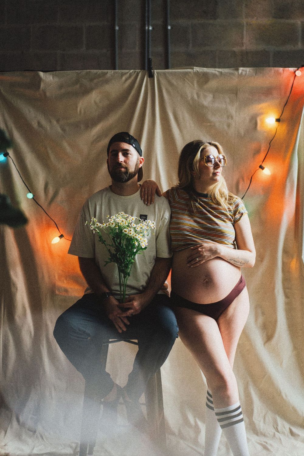 Artistic portrait against white backdrop with string lights and floral elements creating moody atmosphere.