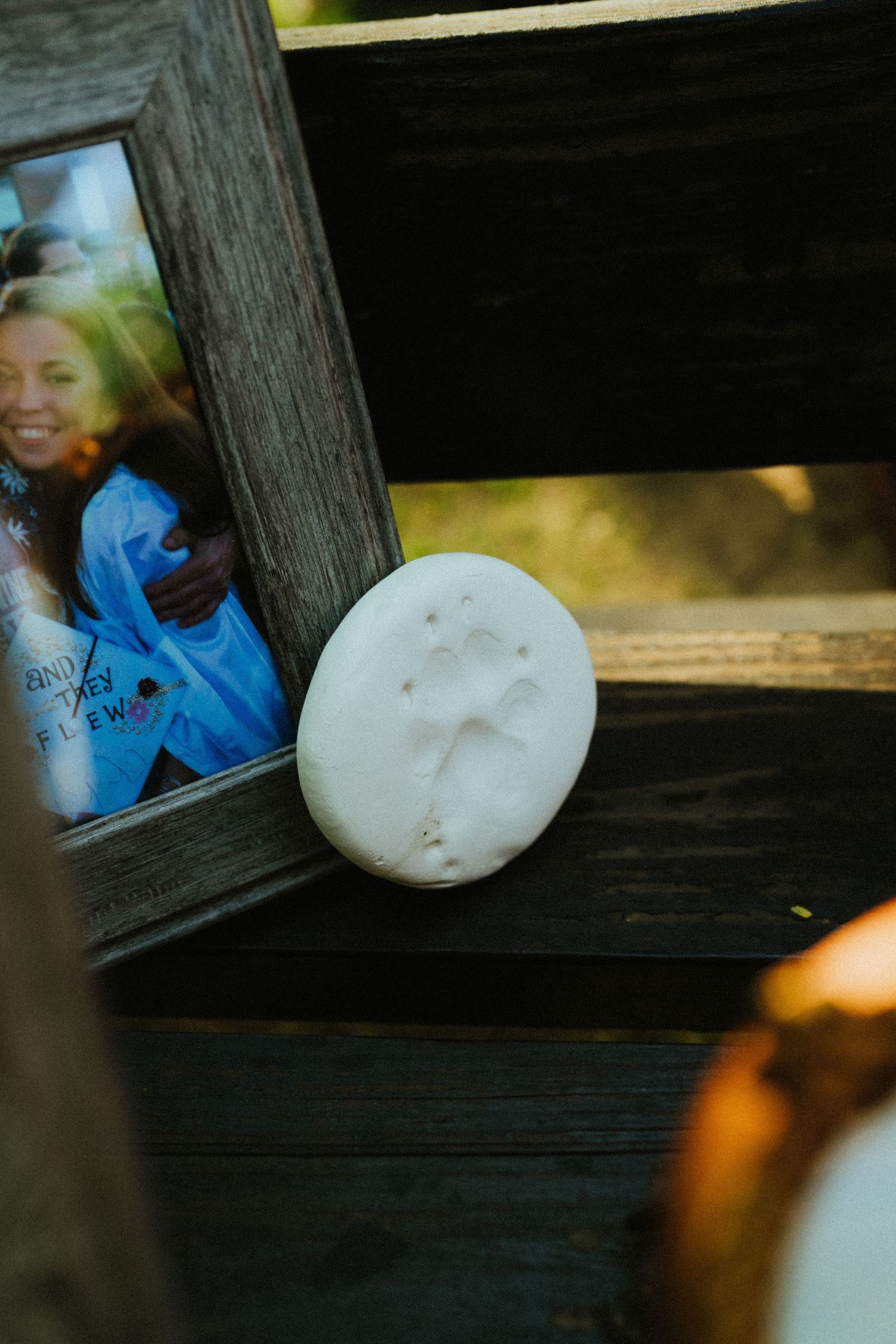 White clay handprint keepsake on wooden bench beside rustic photo frame with smiling people.