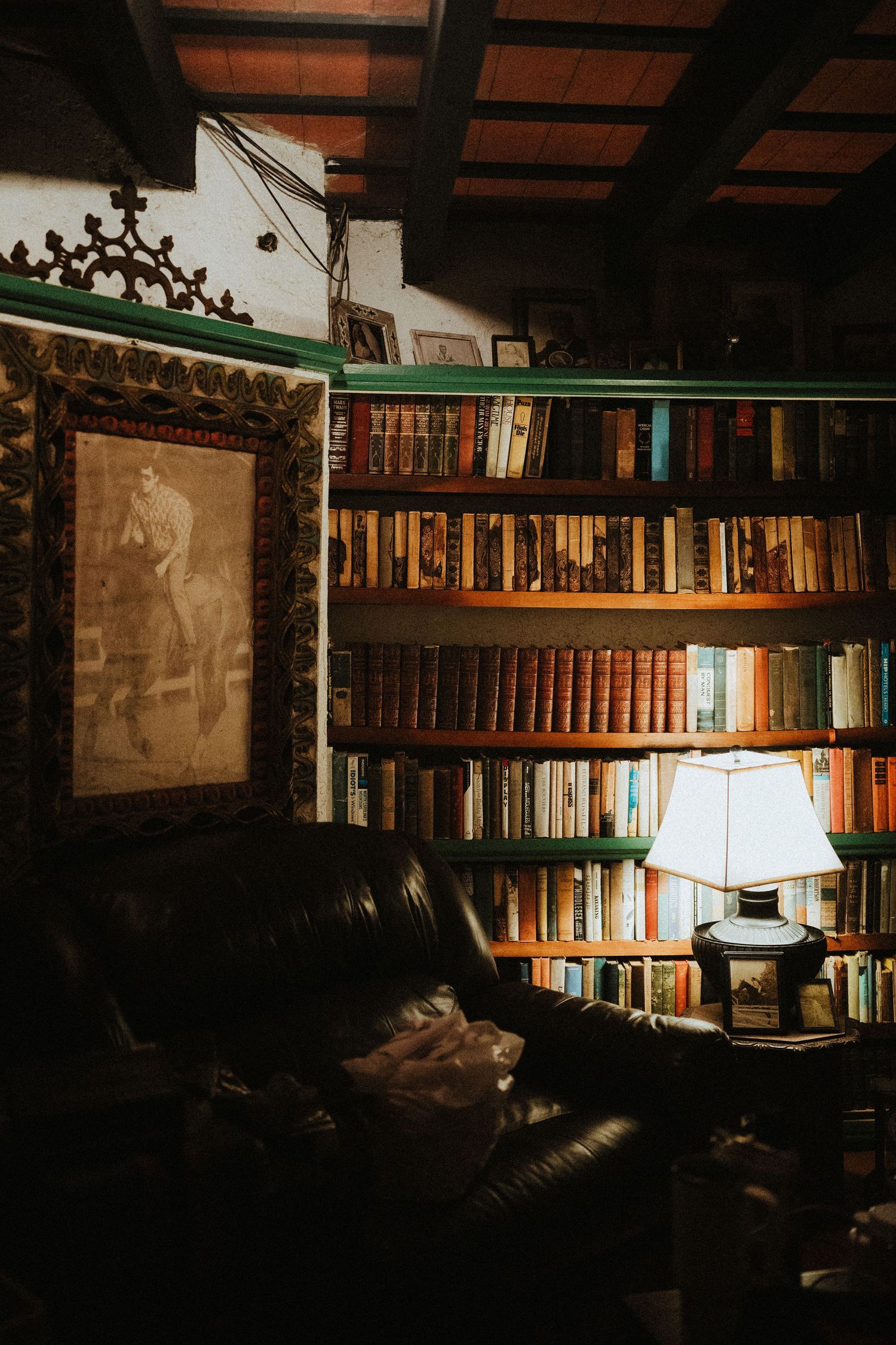 Cozy vintage library with leather armchair, glowing table lamp, and floor-to-ceiling bookshelves beside an ornate framed portrait.