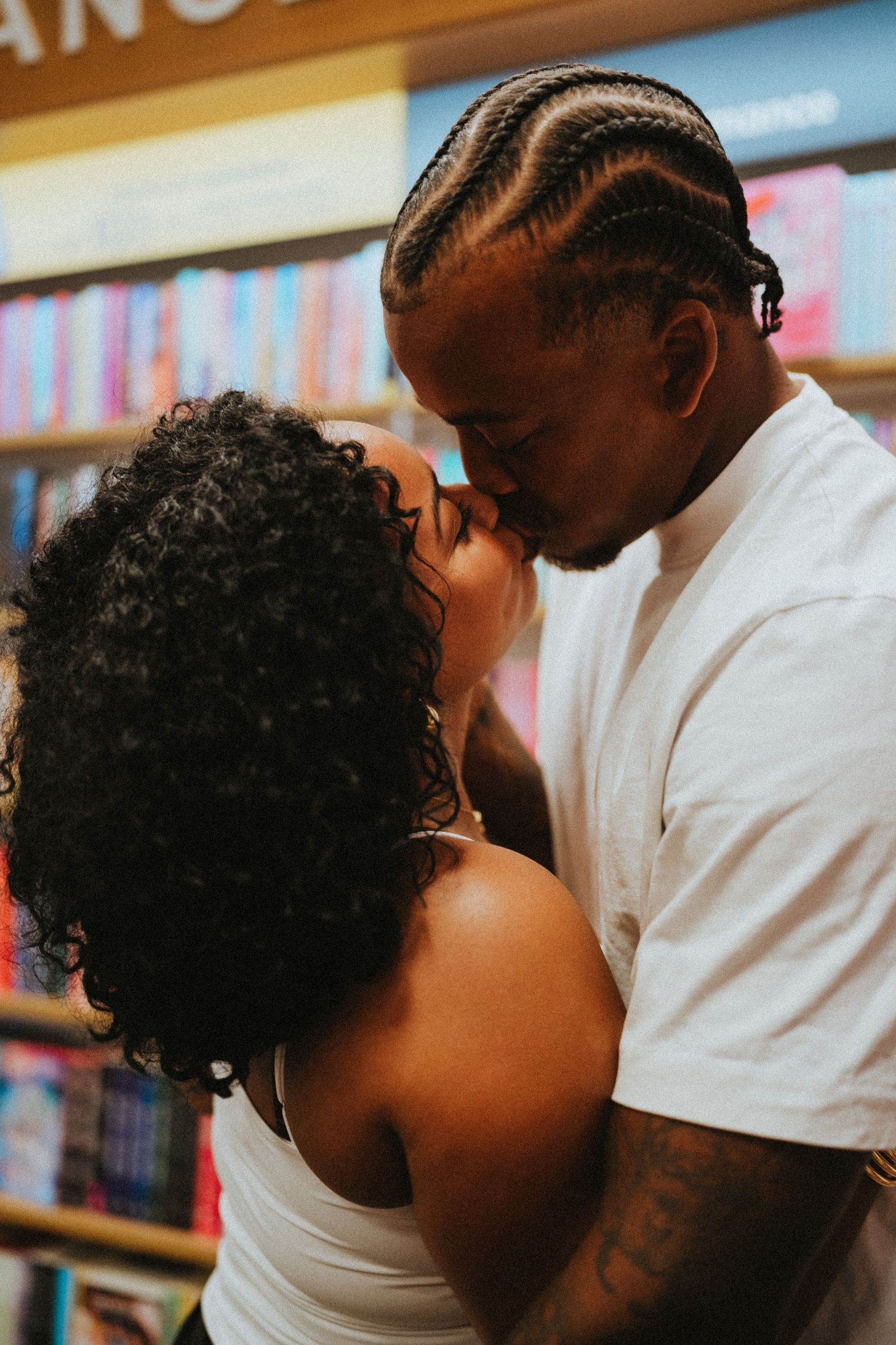 Couple sharing a romantic kiss in a bookstore with colorful shelves in the background.
