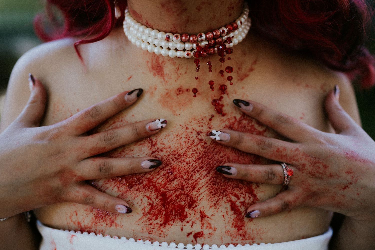 Woman in white dress with pearl choker necklace, hands on chest covered in red glitter for Halloween costume.