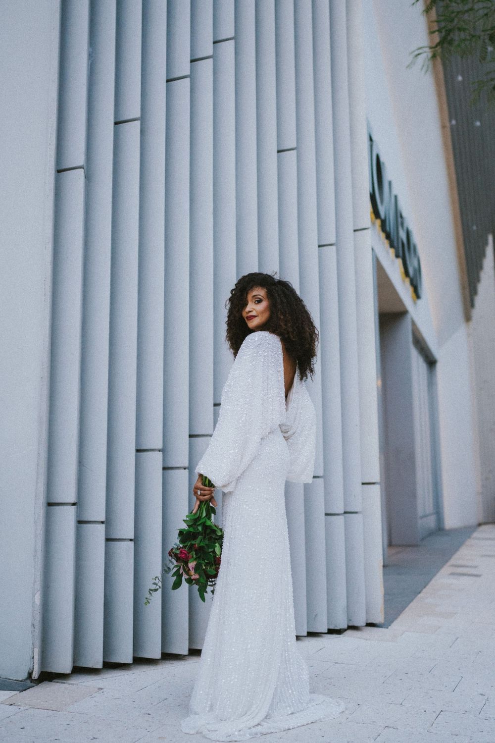 A person in a flowing white dress poses against modern architectural columns.