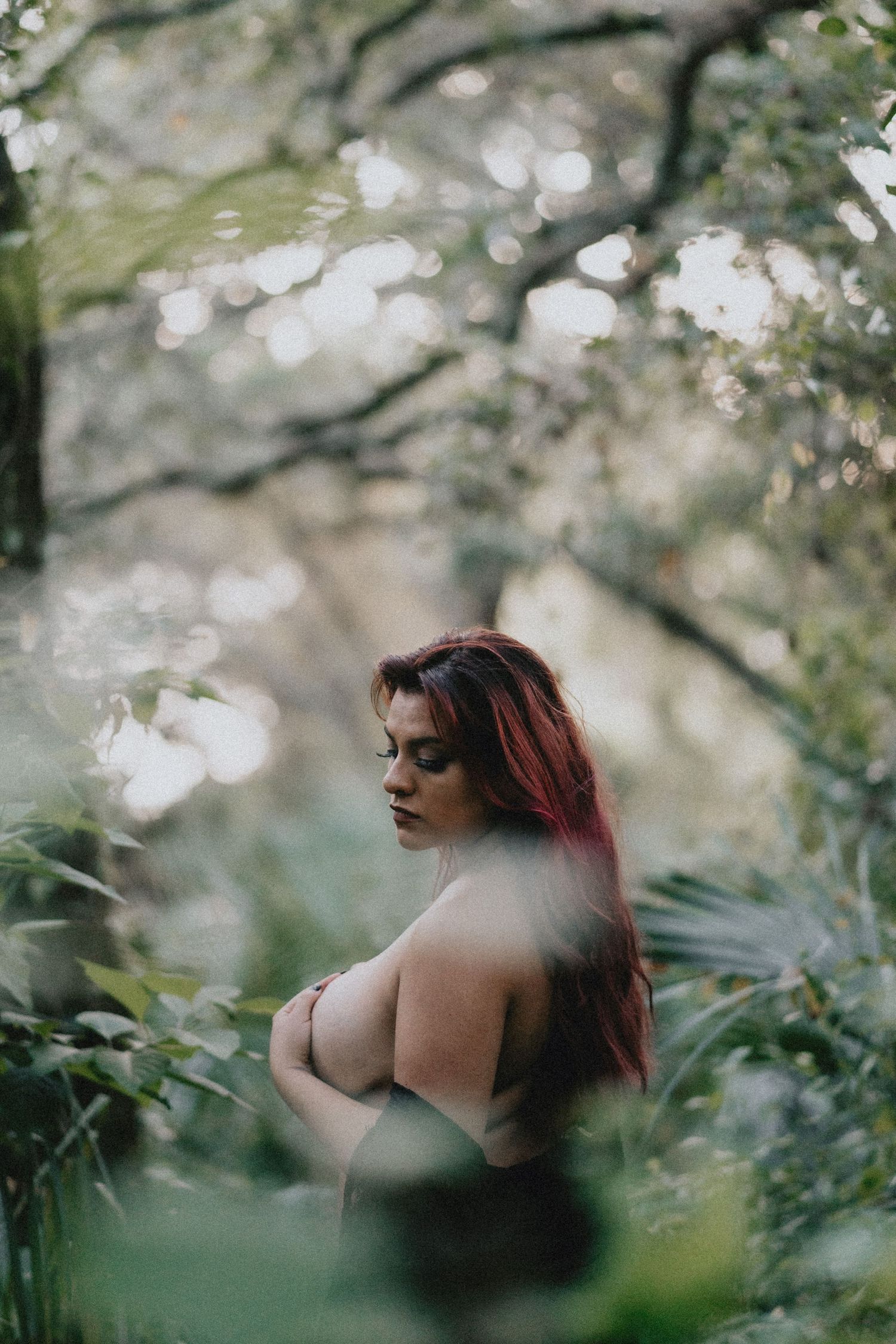 Artistic portrait through foliage with bokeh lighting effects.