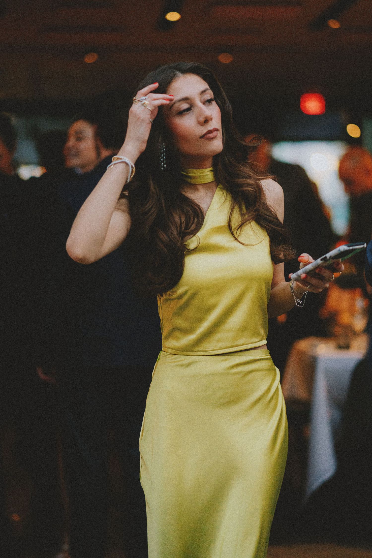 Woman in yellow satin dress holding phone at elegant evening event.