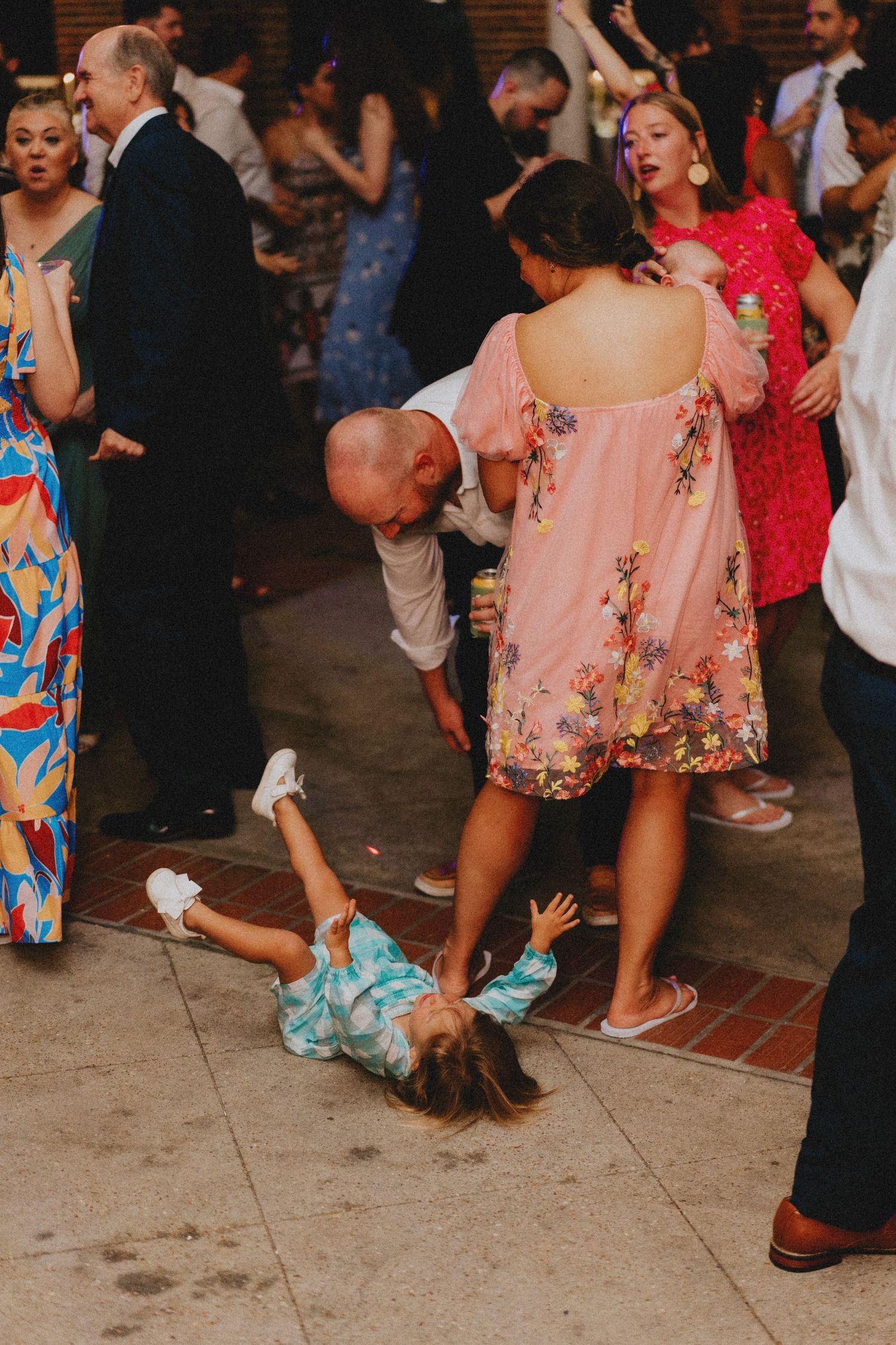 Wedding guests dance and mingle on a brick patio during an outdoor reception celebration.