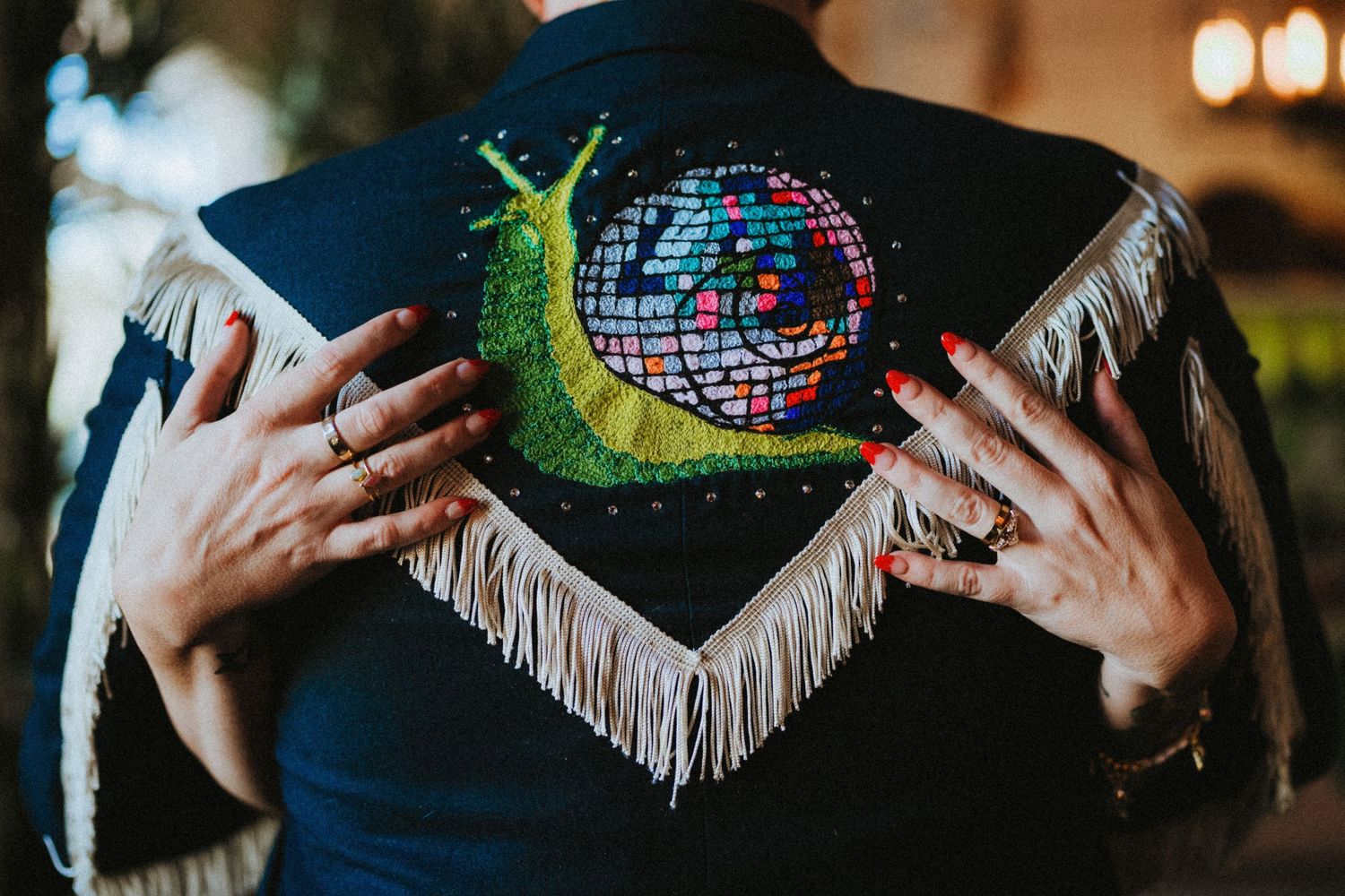 Close-up of a black fringed jacket with colorful embroidered snail and disco ball design on the back.