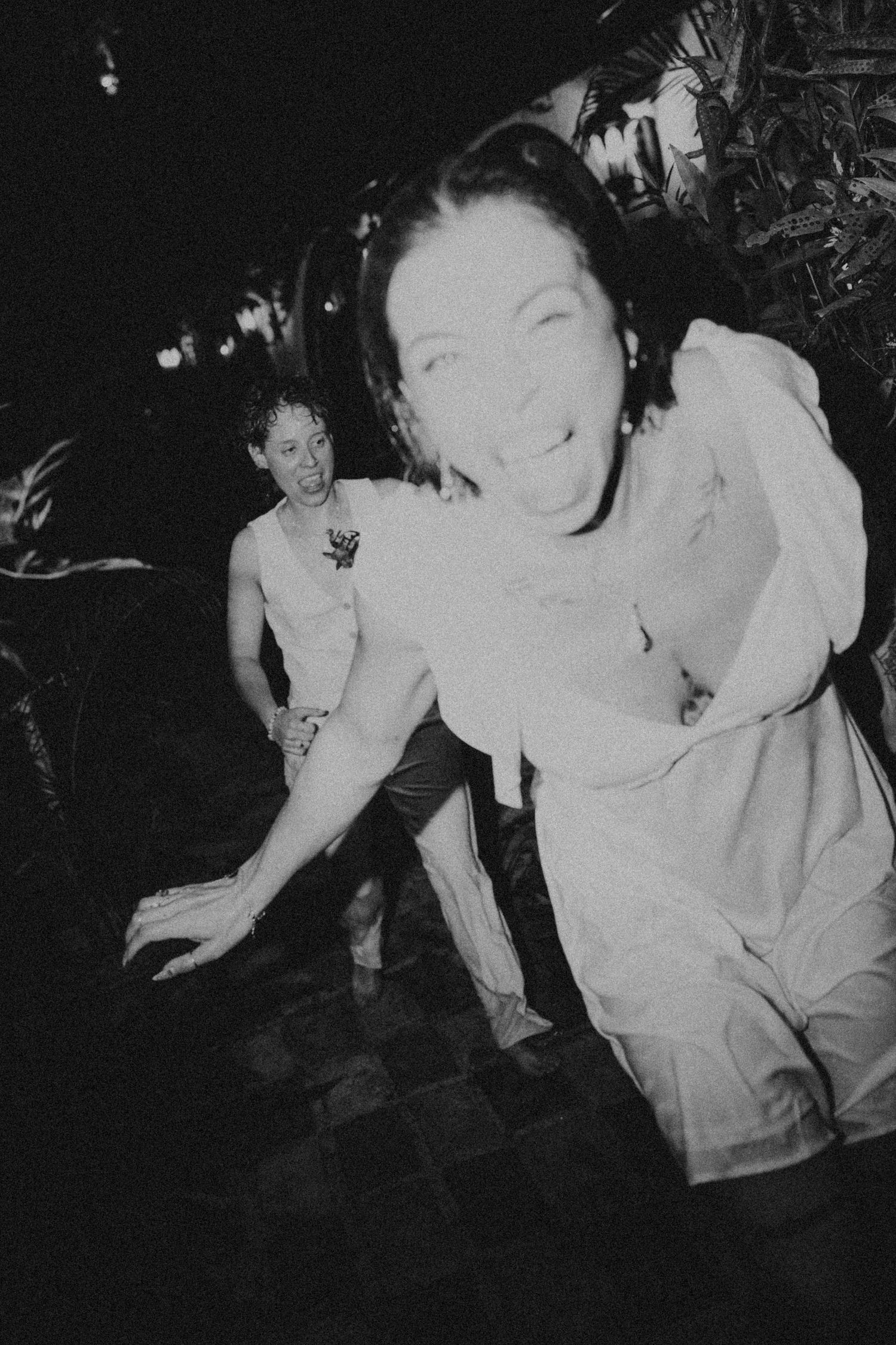 Black and white photo of two people laughing and dancing outdoors at a nighttime party event.