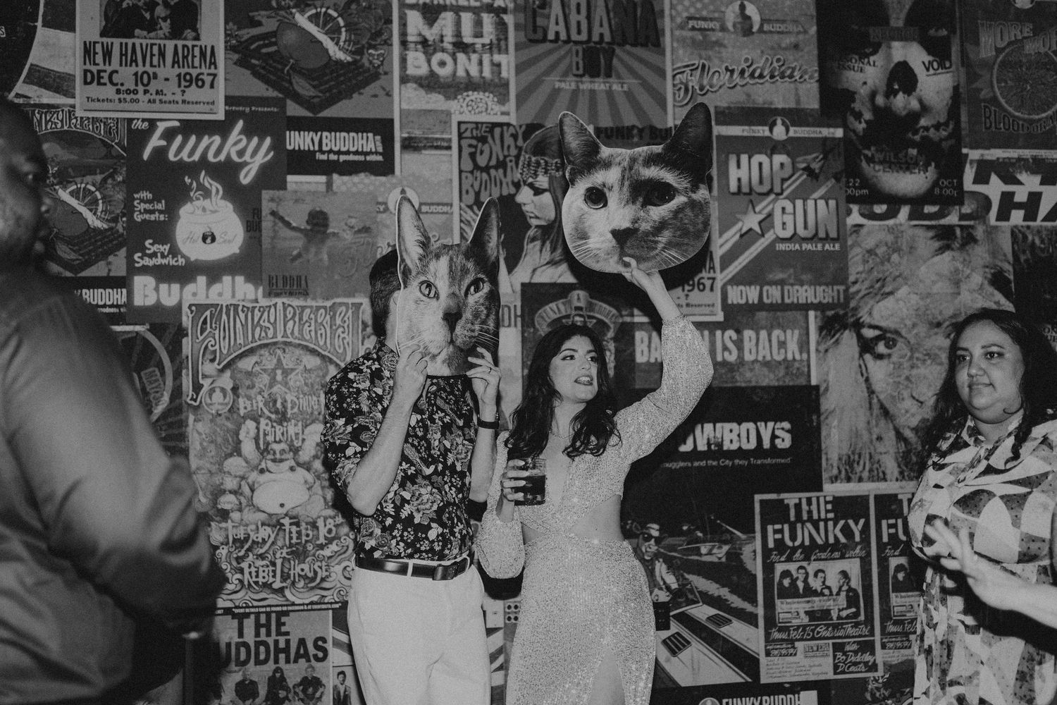 Black and white photo of a bride posing with animal masks against a wall of concert posters.