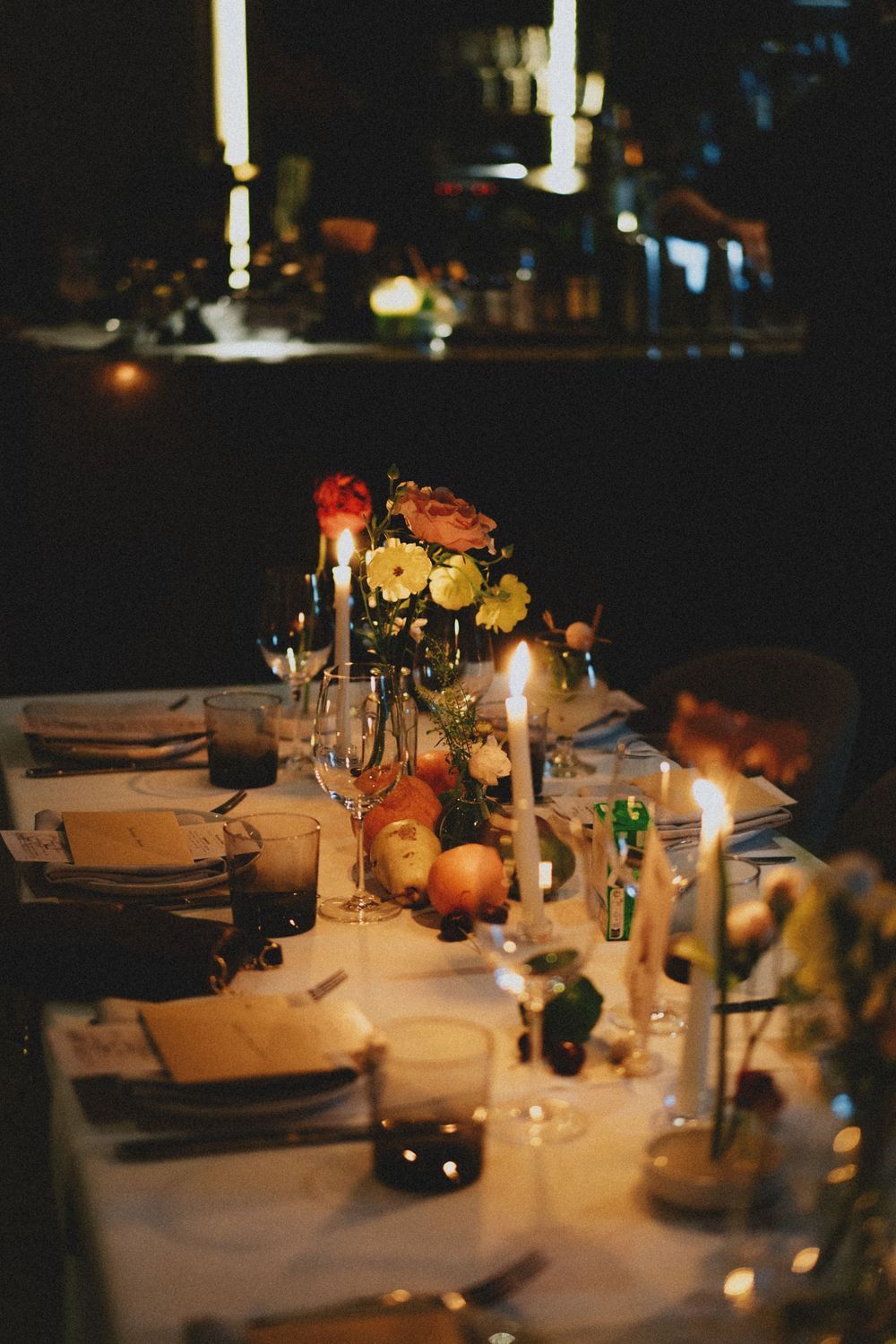 Wedding reception table decorated with autumn fruits, flowers, and candlelight in warm ambient lighting.