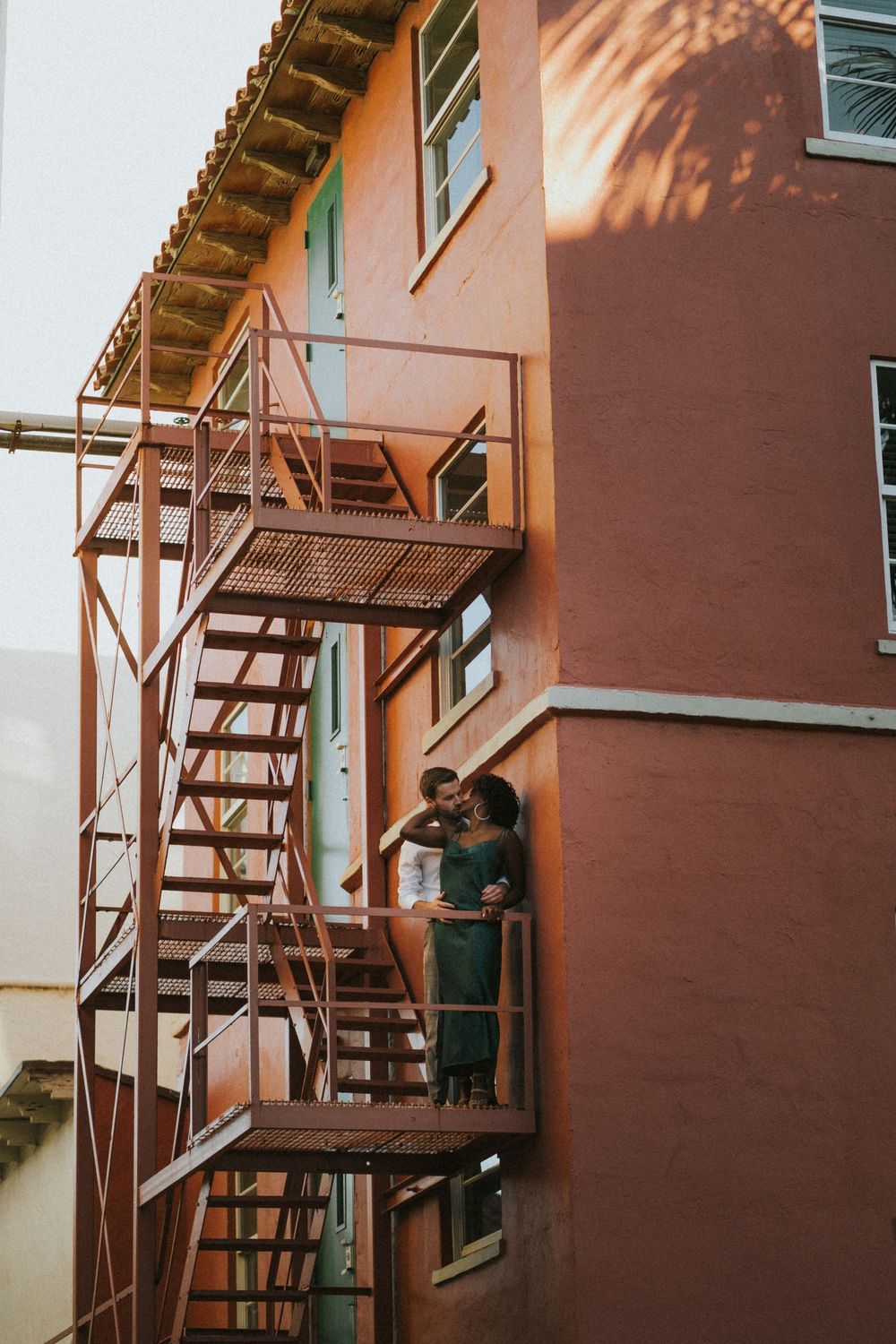 Creative photoshoot on rustic metal staircase against terra cotta colored building exterior.