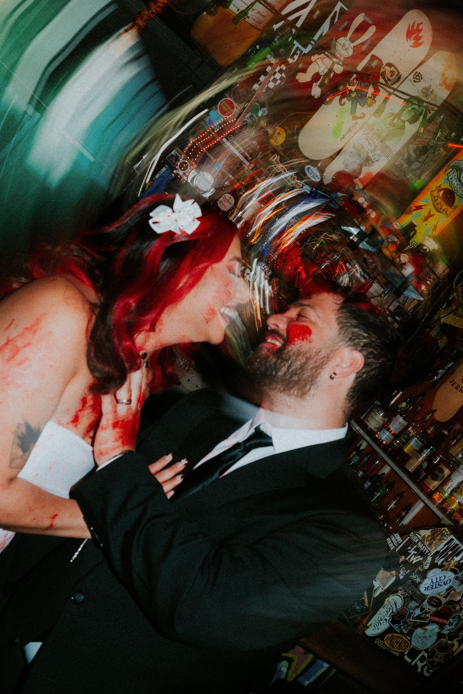 Bride with red hair and groom in black suit share a dramatic kiss covered in red paint indoors.