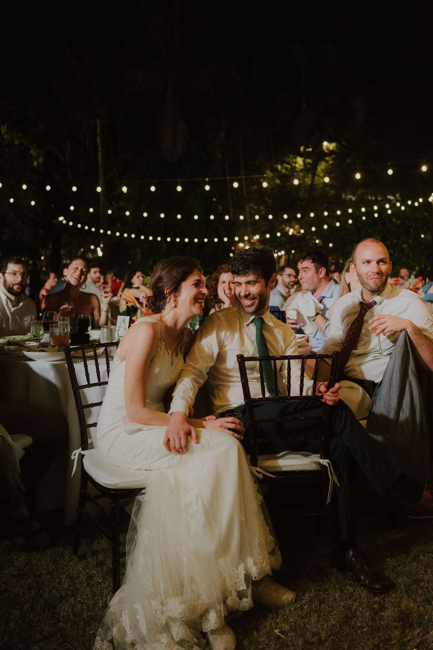 Wedding reception guests dance under romantic string lights at an outdoor evening celebration.