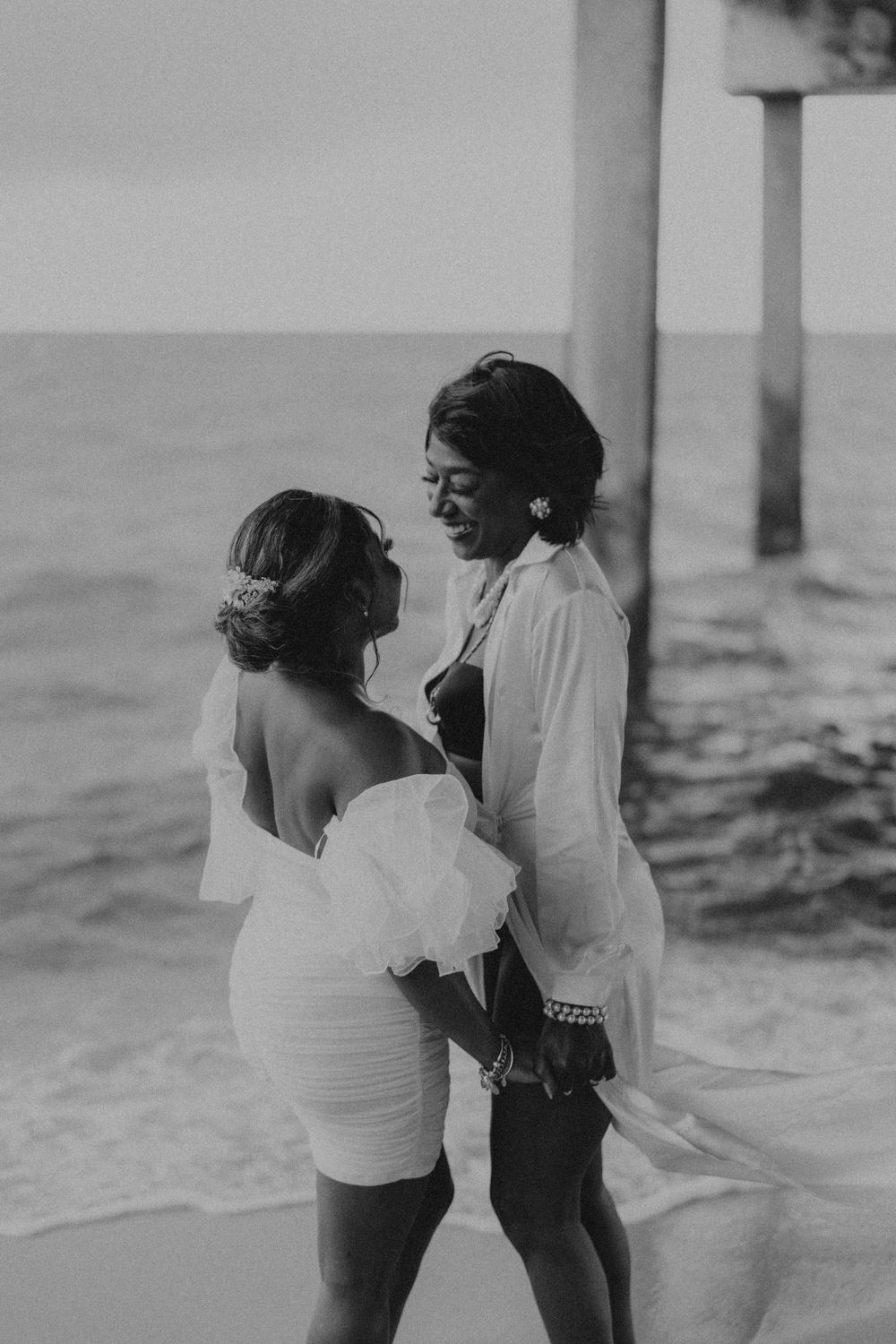Black and white photo of couple embracing on a beach at sunset.