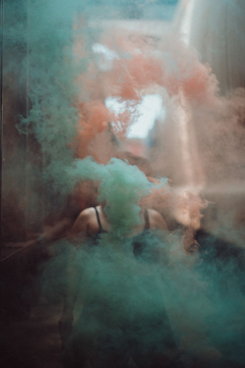 Colorful smoke bombs creating ethereal turquoise and coral clouds in atmospheric scene.