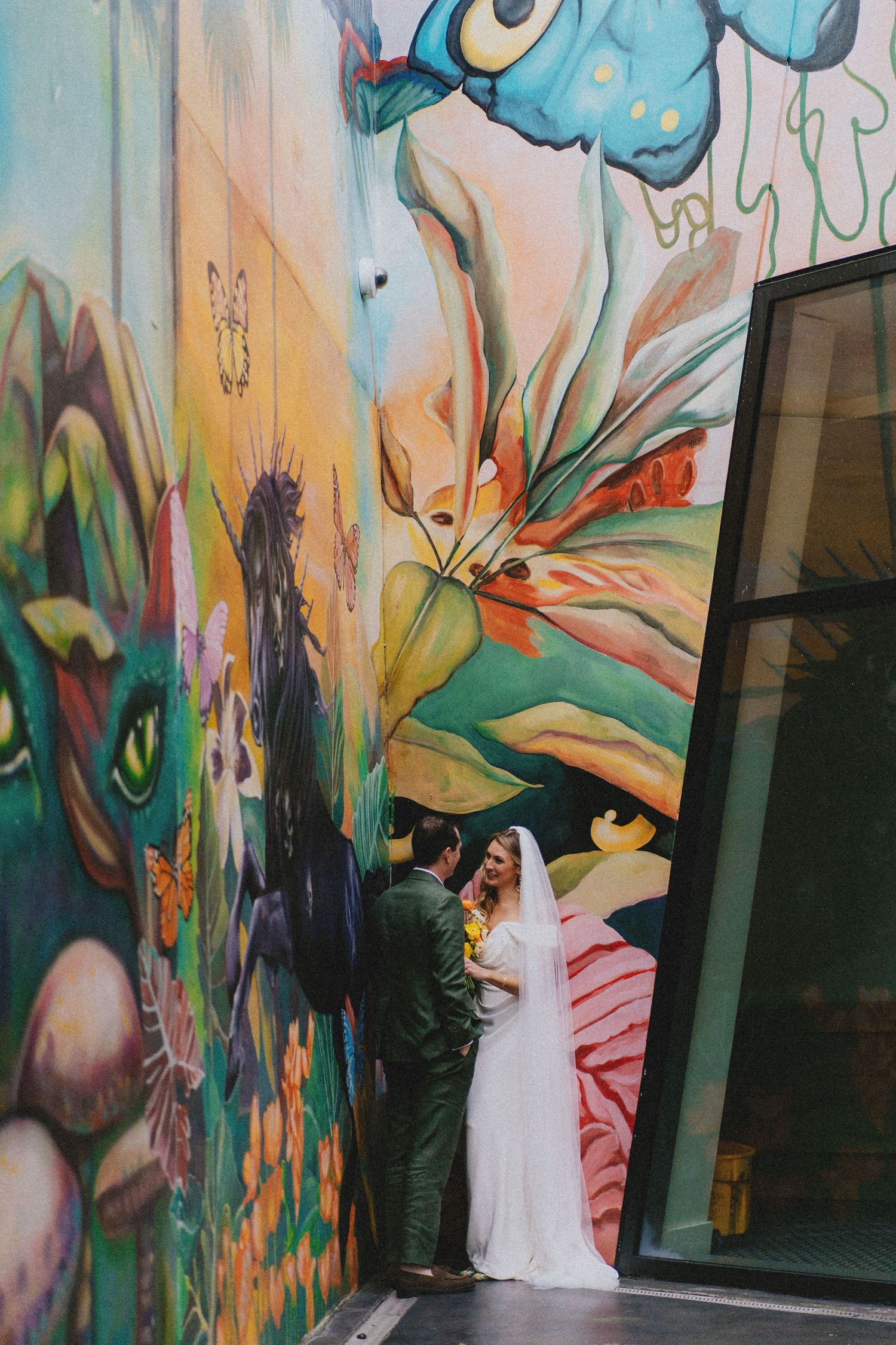 Bride and groom sharing an intimate moment in front of a vibrant colorful street art mural.